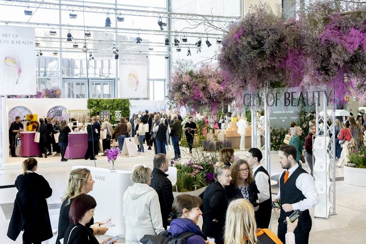 City of Beauty im Glasfoyer Besucherinnen und Besucher im Glasfoyer der Messe Düsseldorf bei The Art of Beauty & Health, mit floraler Dekoration und „City of Beauty“-Schriftzug.