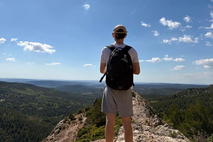 Aussicht von der Montagne Sainte-Victoire Victor steht auf einem Berg mit Rucksack steht mit dem Rücken zur Kamera vor einer weiten Aussicht