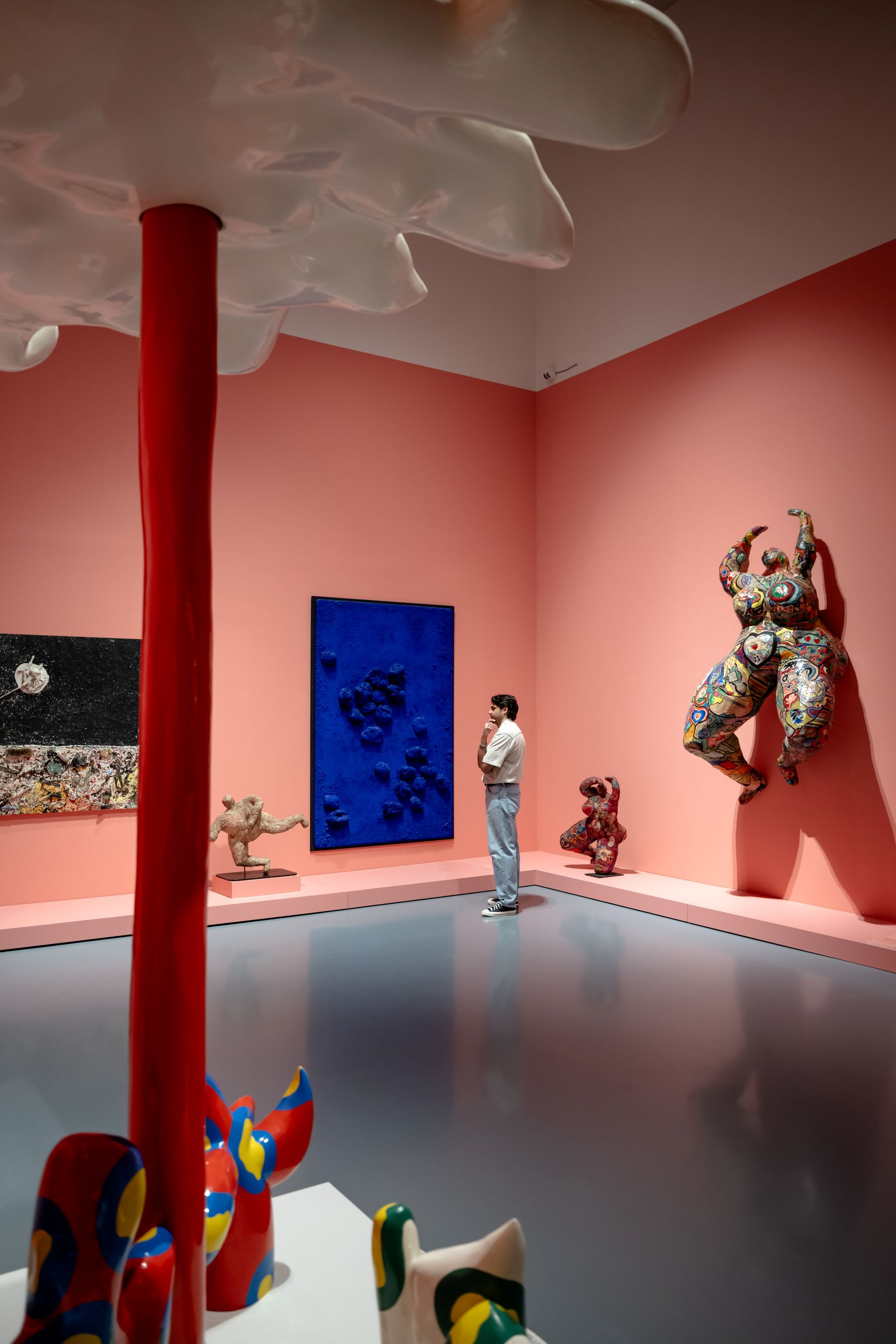 Blick in einen rosafarbenen Raum der Ausstellung Dream Machine. In der Mitte hängt das blaue Schwammrelief von Yves Klein, rechts eine große Nana von Niki de Saint Phalle.