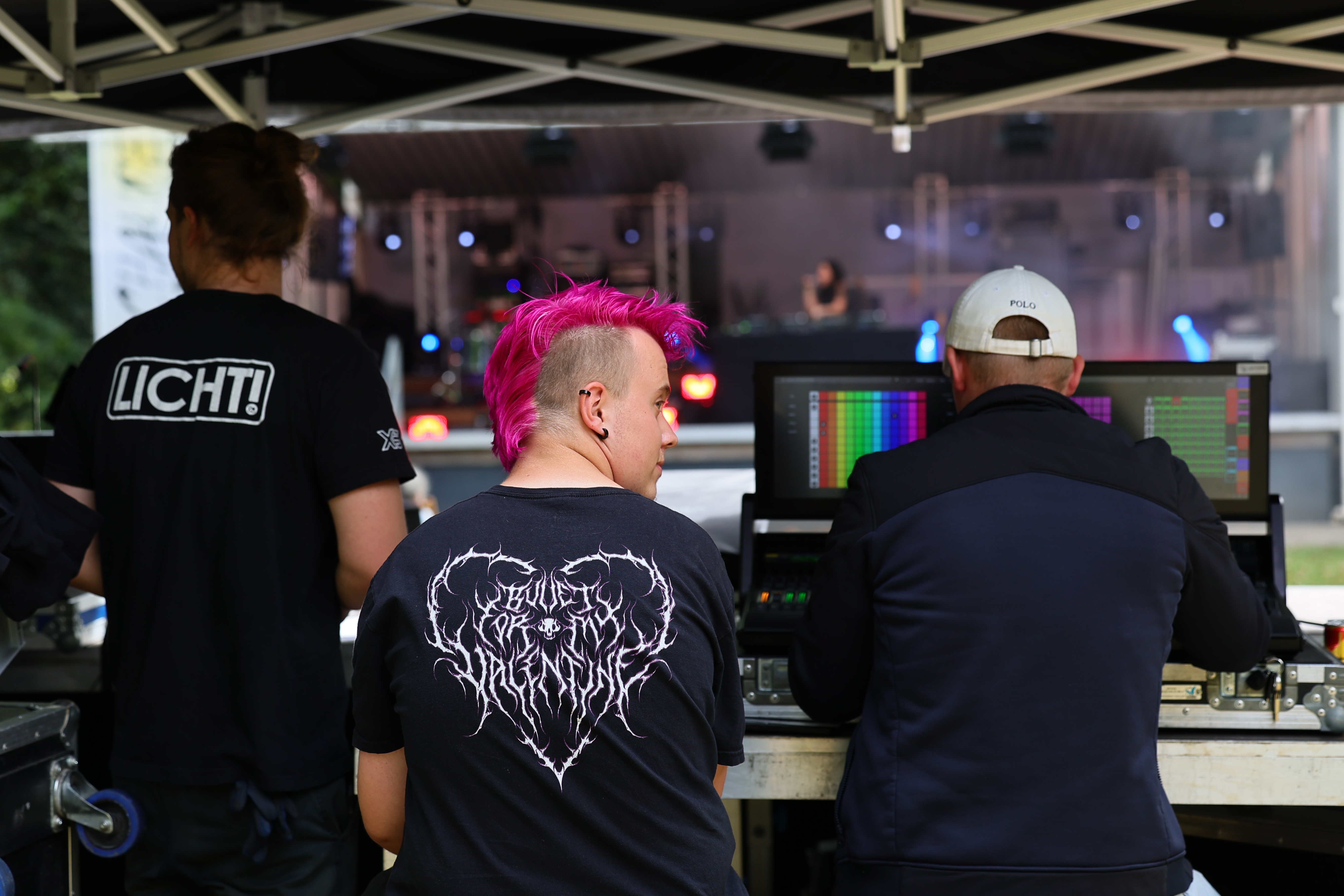 Drei Personen arbeiten an Mischpulten unter einem Technikzelt vor der Bühne