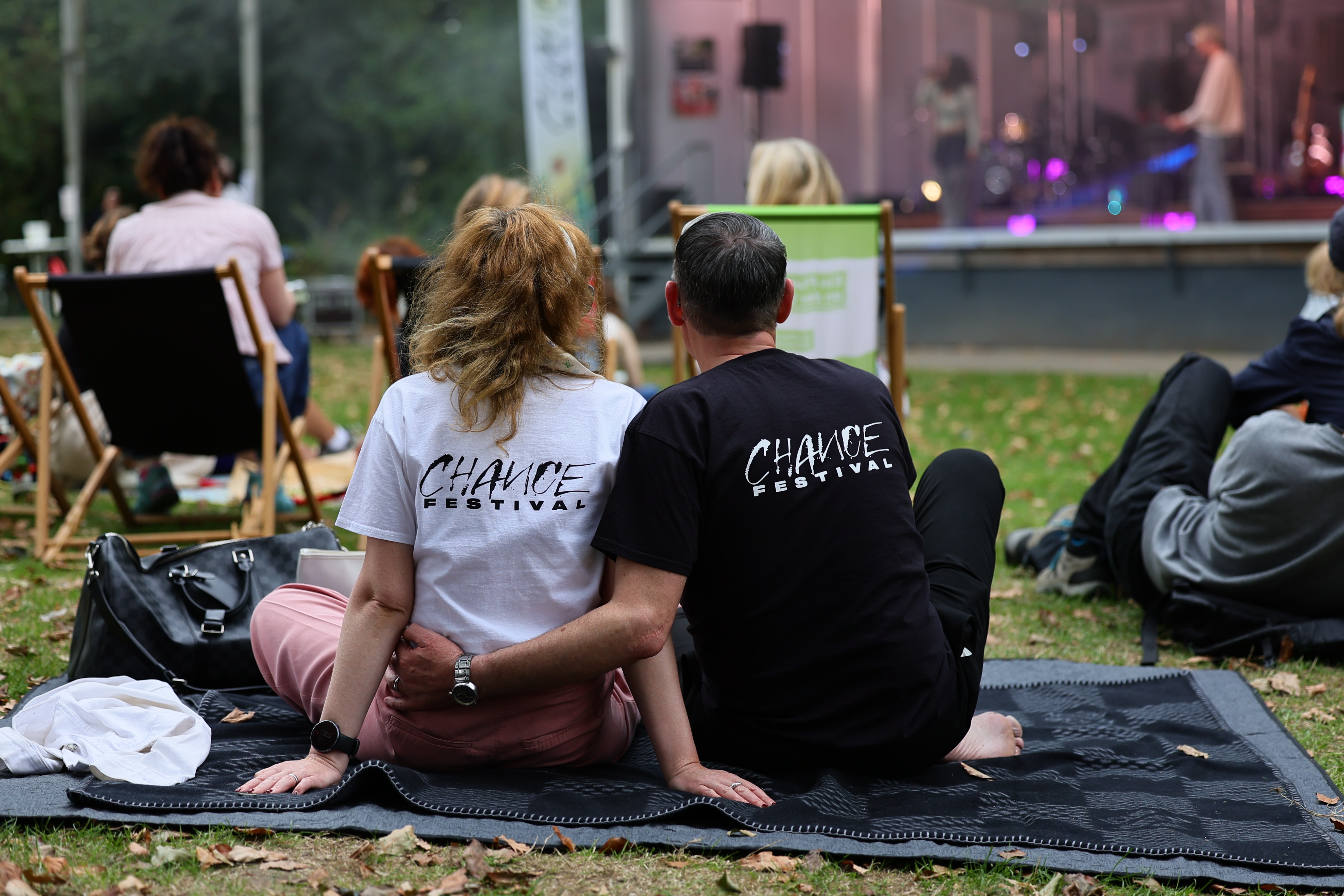 Zwei Menschen mit CHANCE-Shirts sitzen gemeinsam auf einer Decke und schauen zur Festivalbühne