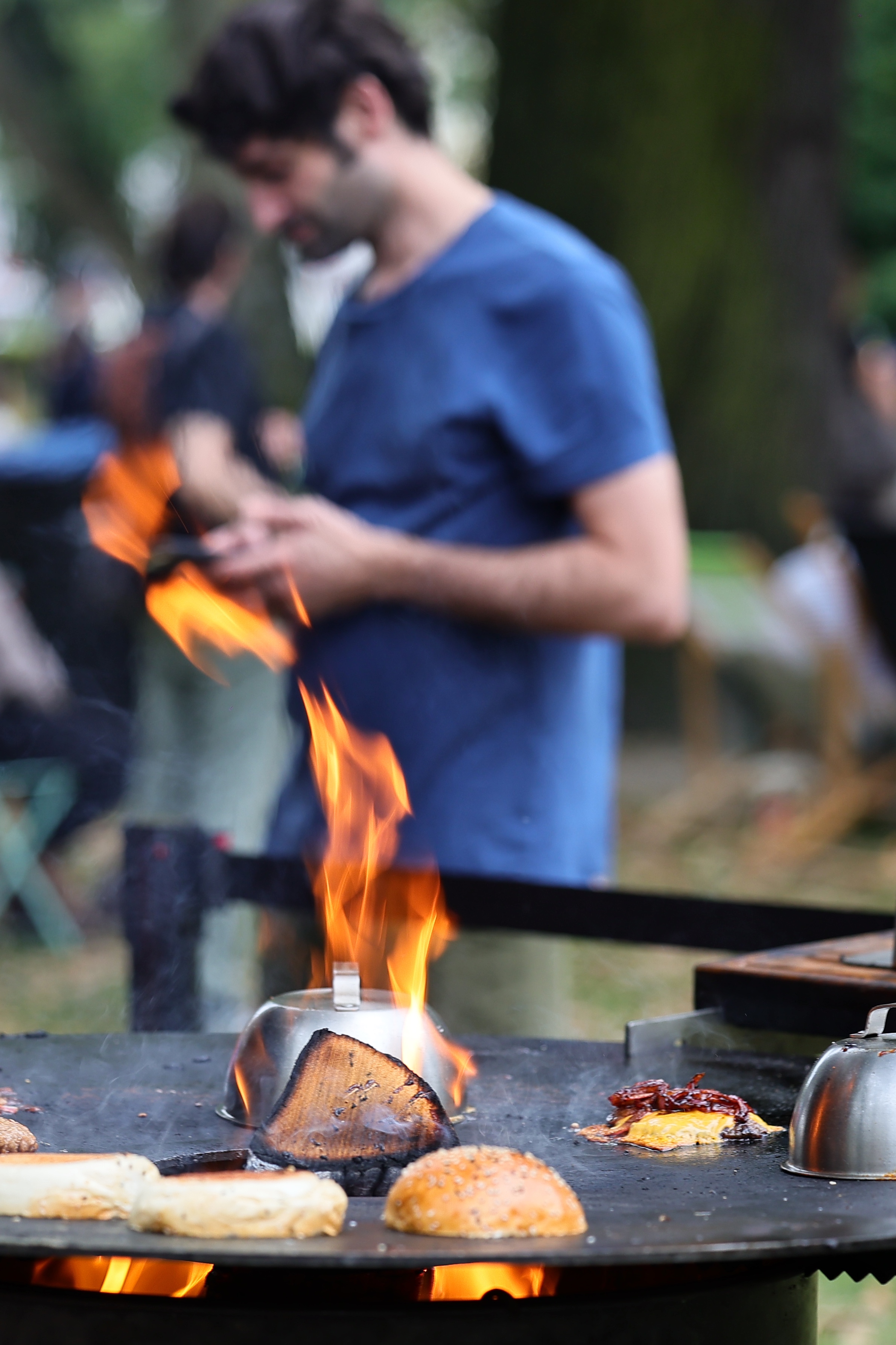 Ein Mann bereitet Burger auf einer offenen Feuerplatte zu