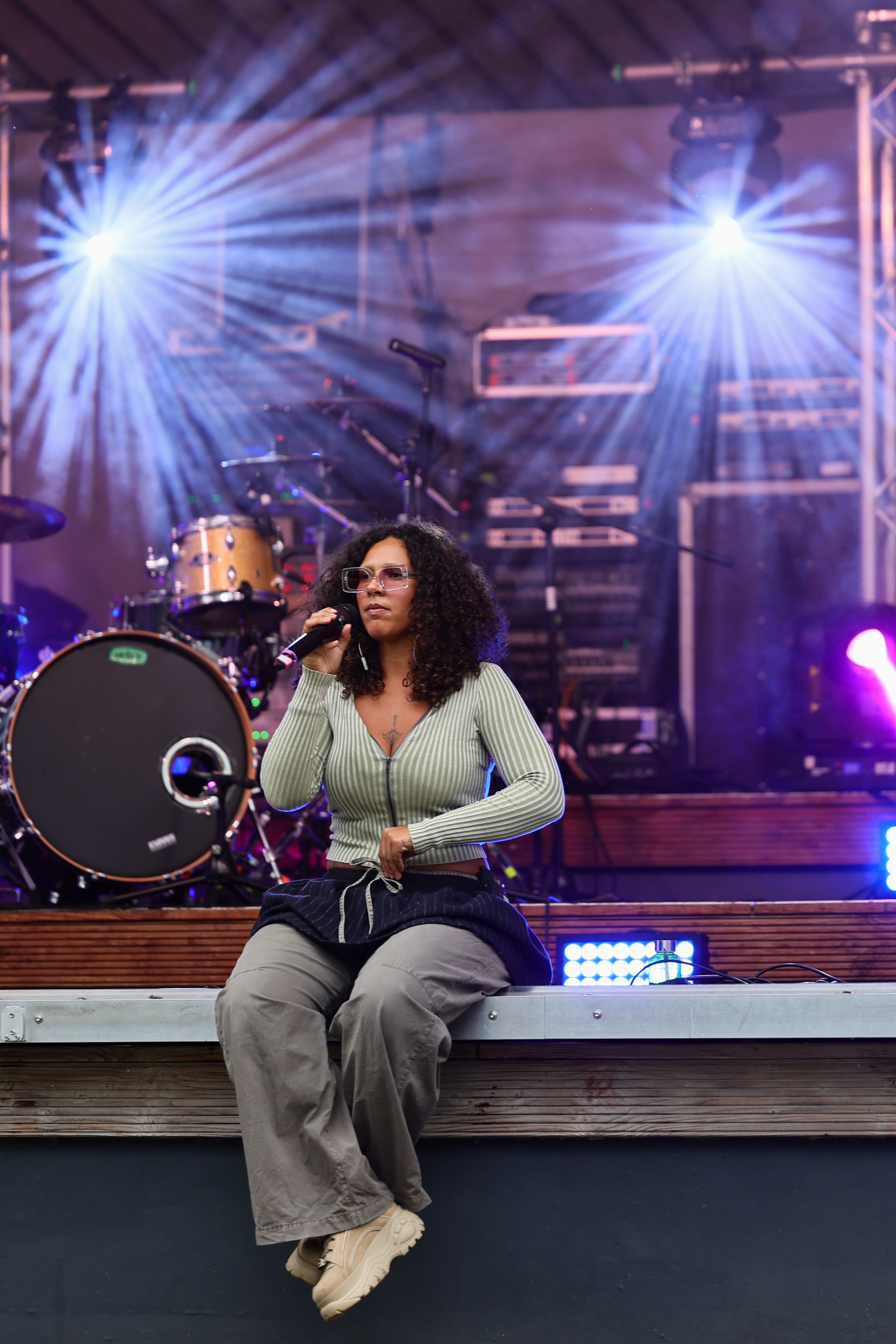 Mauvaise Bouche sitzt mit einem Mikrofon am Rand der Bühne des CHANCE Festivals