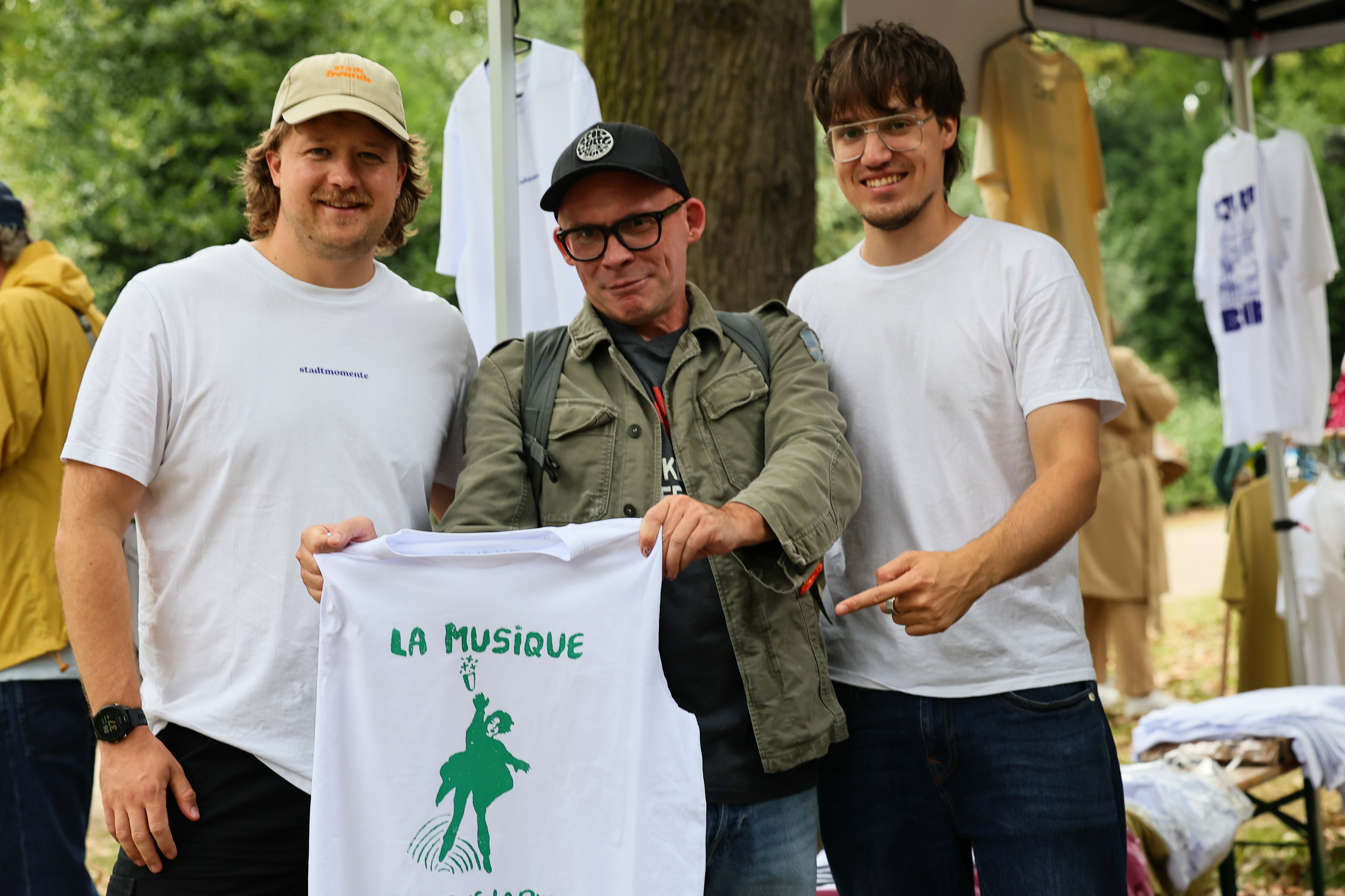 Drei Männer zeigen ein frisch bedrucktes weißes T-Shirt mit grünem Motiv