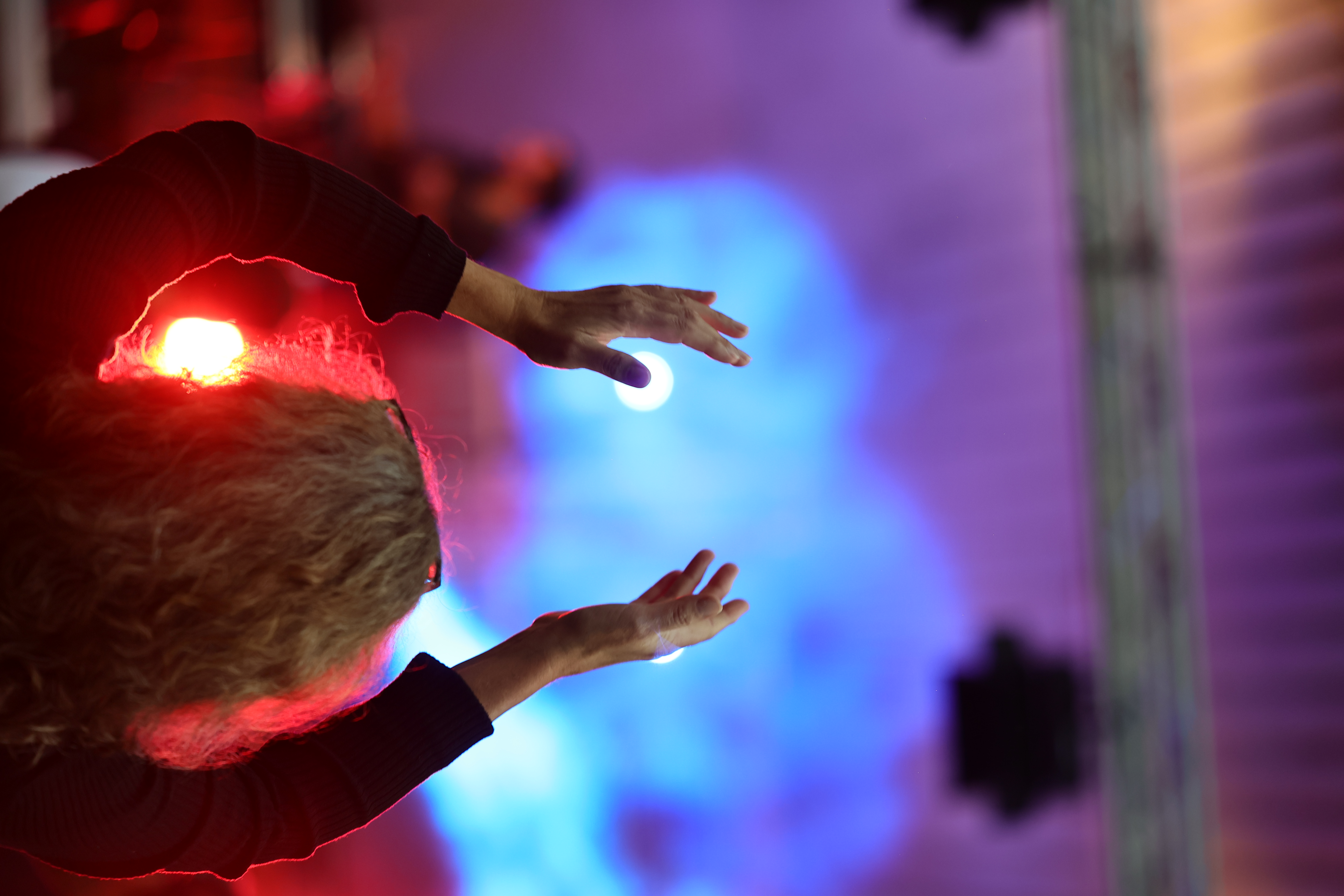 Eine Person hebt vor einer farbig beleuchteten Festivalbühne beide Hände