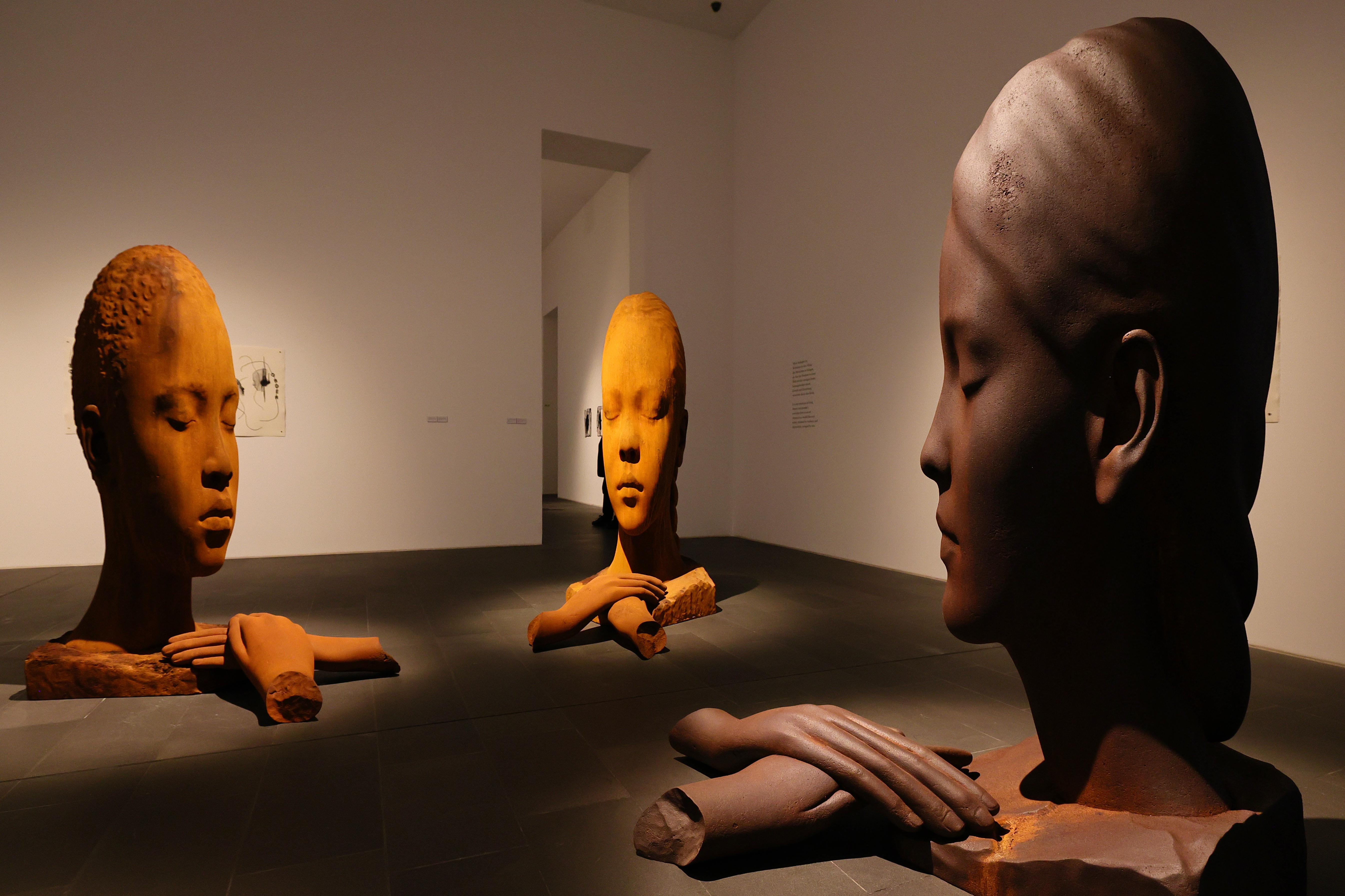 Drei Kopfskulpturen von Jaume Plensa mit geschlossenen Augen, langen Hälsen und vor dem Körper liegenden Händen im Museum Küppersmühle