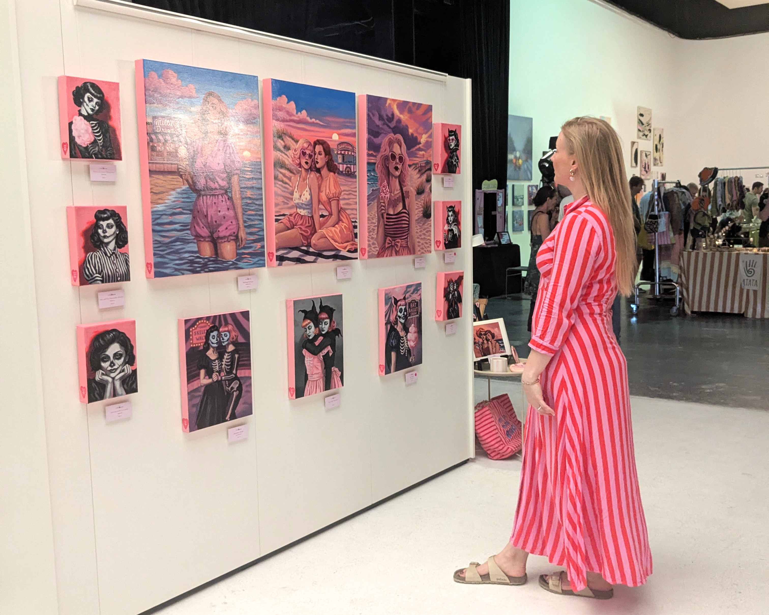 Besucherin in einem rot-pink gestreiften Kleid betrachtet eine Wand mit pinkfarbenen Gemälden