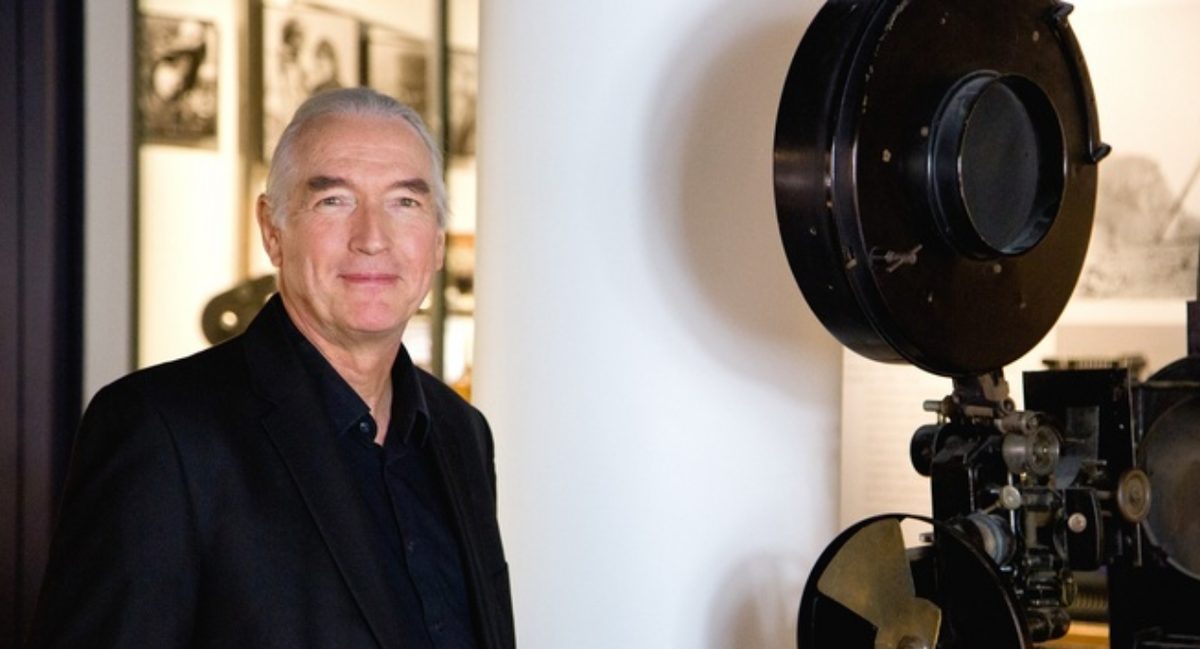 Bernd Desinger im Filmmuseum Düsseldorf Bernd Desinger steht im Filmmuseum Düsseldorf neben historischen Filmprojektoren.