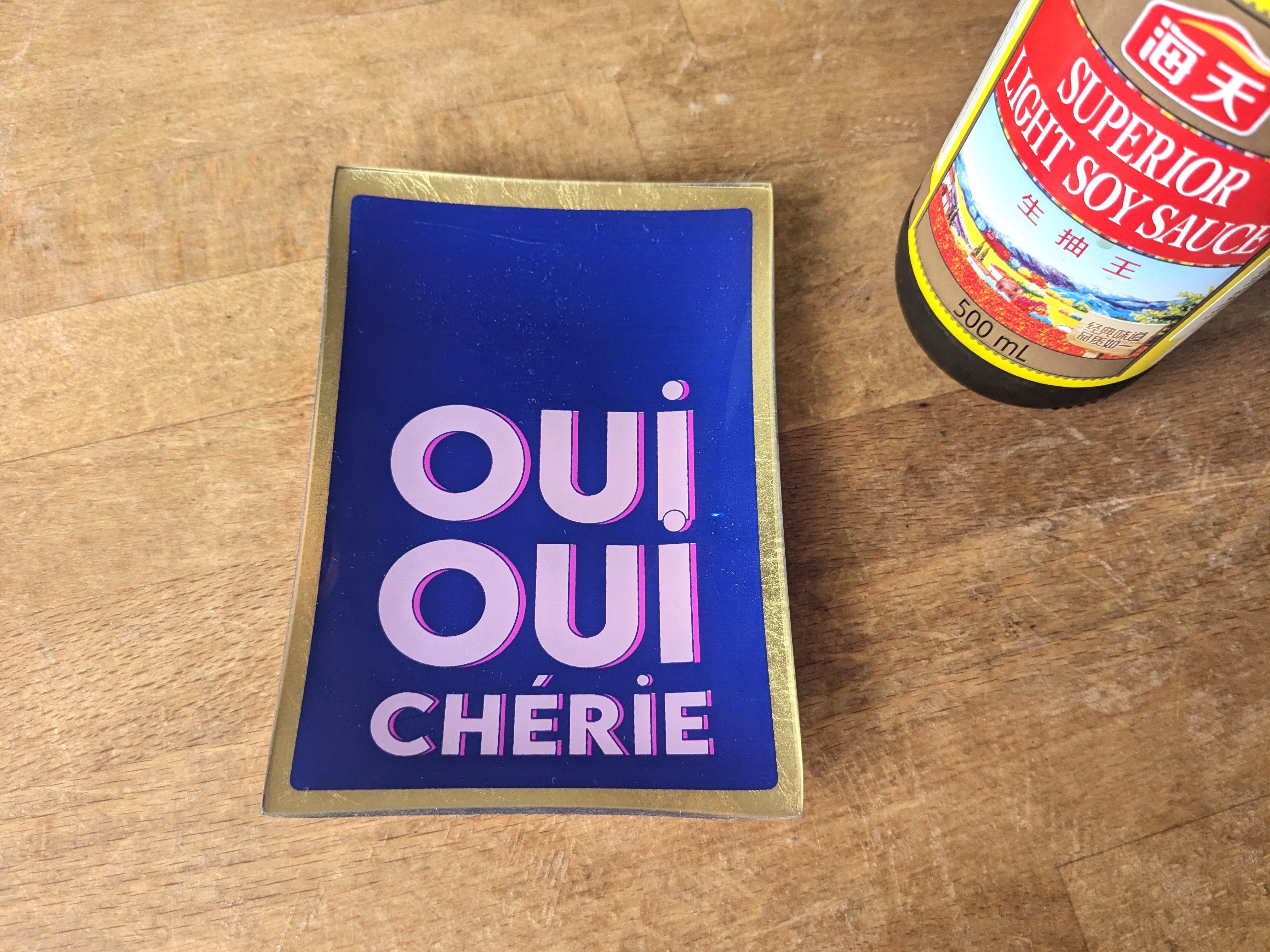 Blaues Glasschälchen mit der Aufschrift Oui oui chérie neben einer Flasche Sojasauce