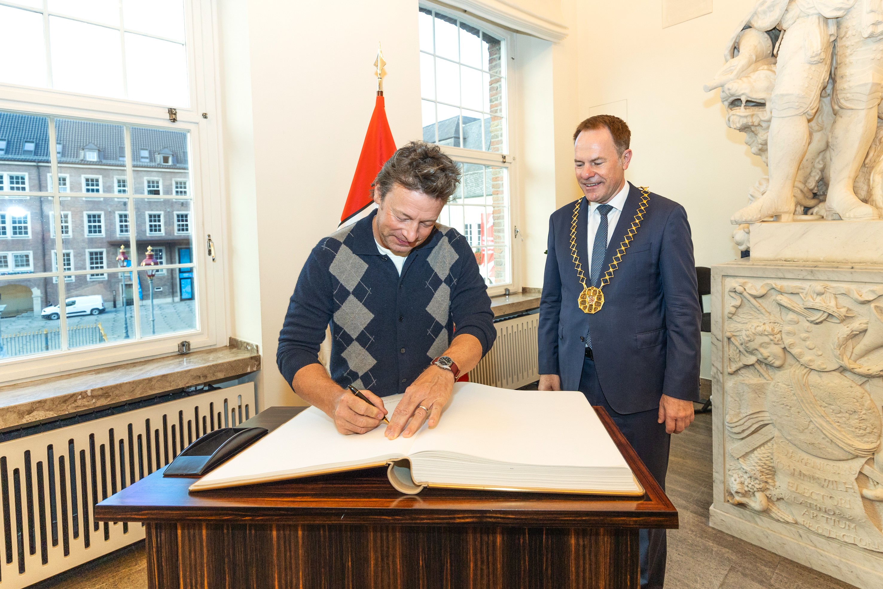 Jamie Oliver unterschreibt im Düsseldorfer Rathaus das Goldene Buch, Oberbürgermeister Stephan Keller steht daneben.