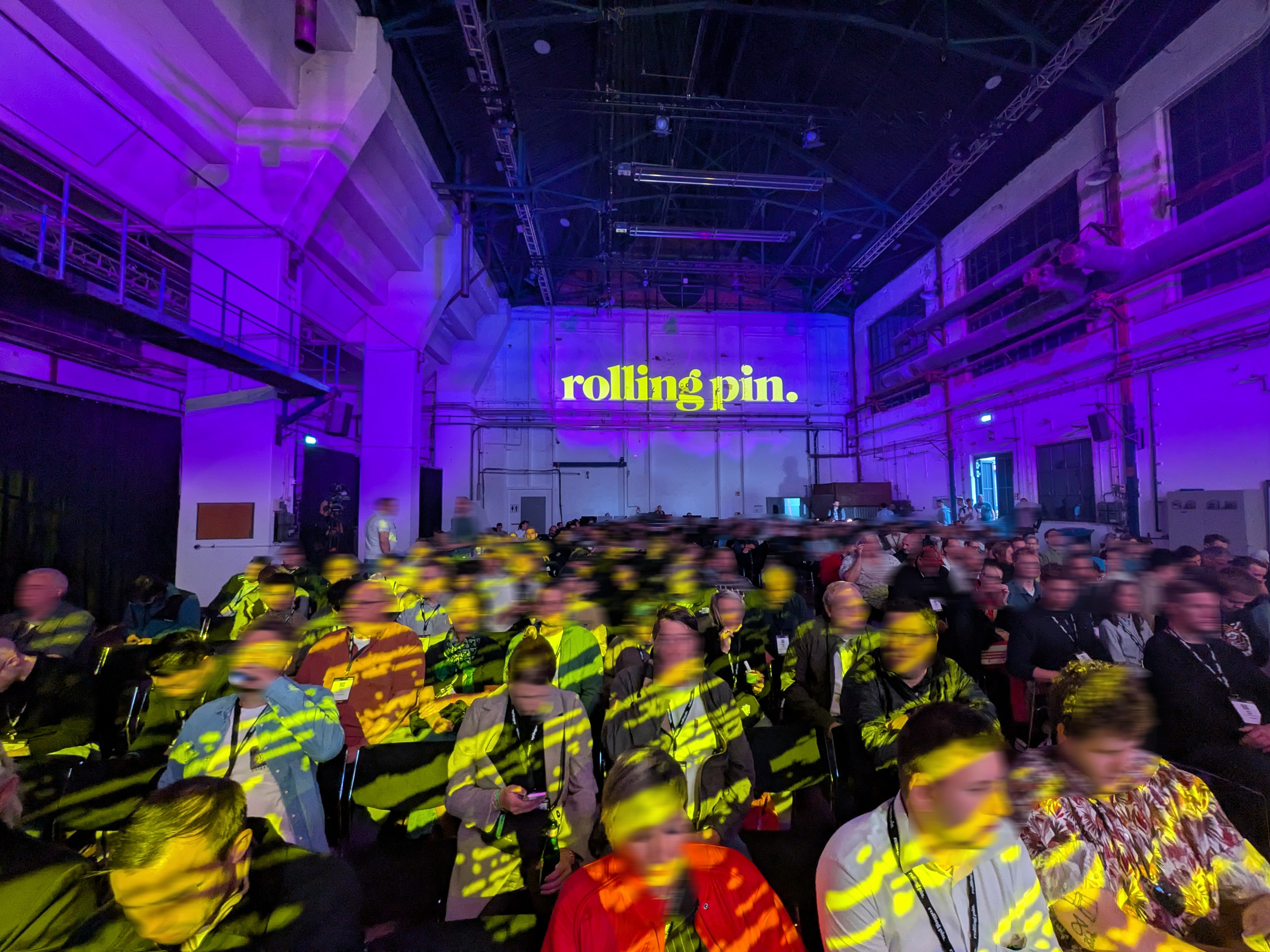 Publikum der Rolling Pin Convention 2025 Besucherinnen und Besucher sitzen unter violett-gelben Lichtprojektionen vor dem Schriftzug „rolling pin.“ im Areal Böhler.