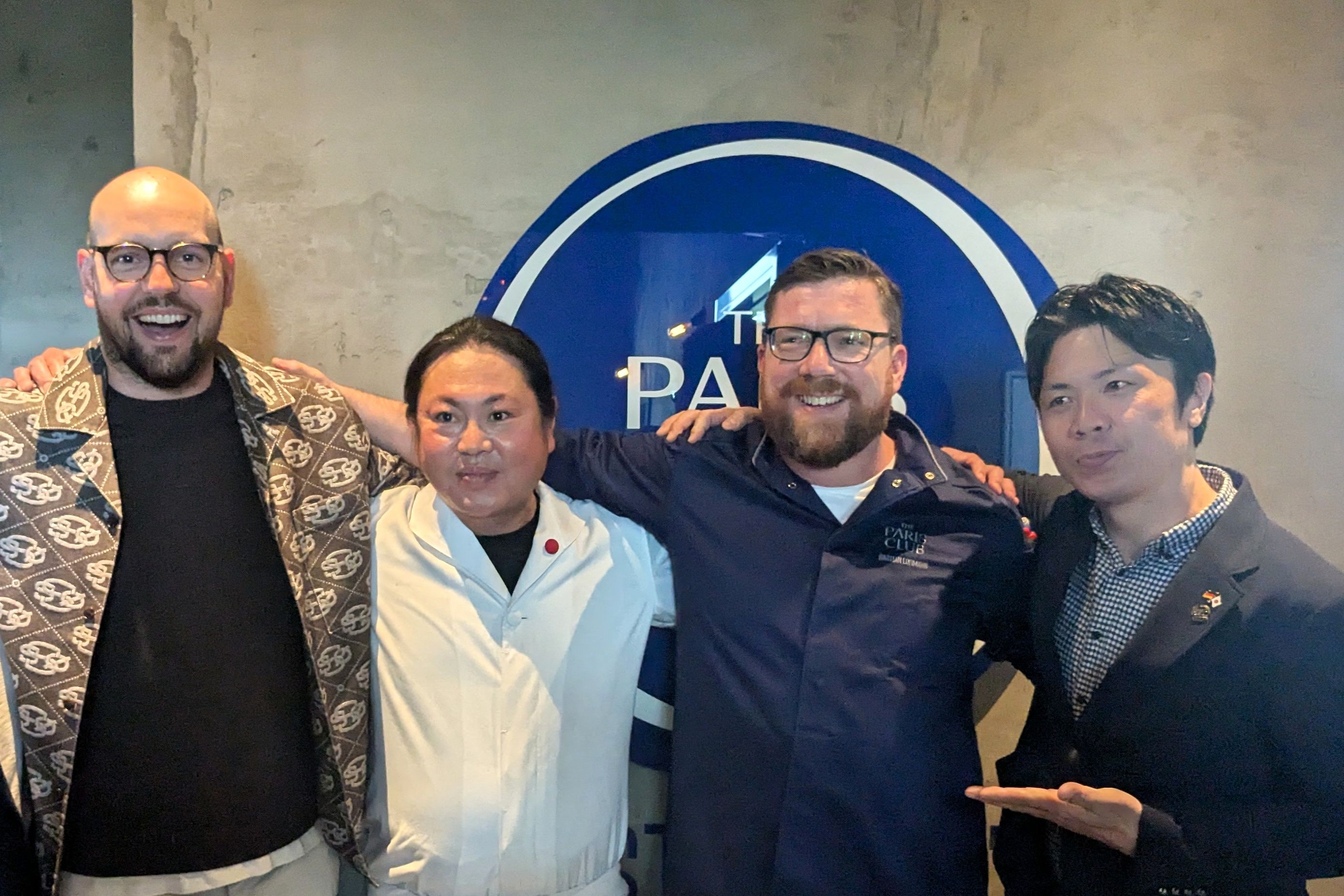 Das Team hinter der Tour de Ramen Gruppenfoto vor dem Logo des The Paris Club Düsseldorf: die Köpfe hinter der Tour de Ramen von TAKUMI und The Paris Club