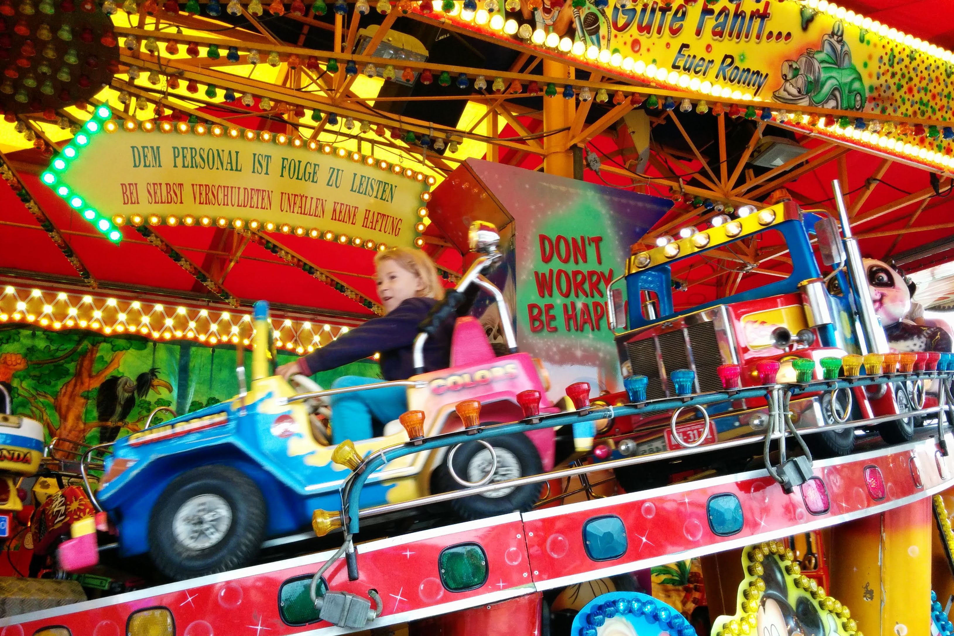 Ein Kind fährt in einem bunten Kinderfahrgeschäft auf der Düsseldorfer Rheinkirmes. Zu sehen sind kleine Fahrzeuge, zahlreiche Lichter und farbig bemalte Kulissen.