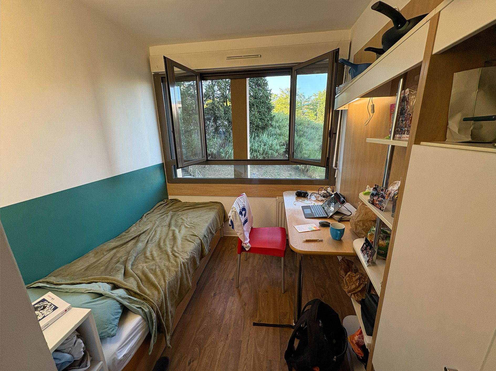 Kleines Zimmer in einem französischen Studierendenwohnheim mit Bett, Schreibtisch und Schrank.
