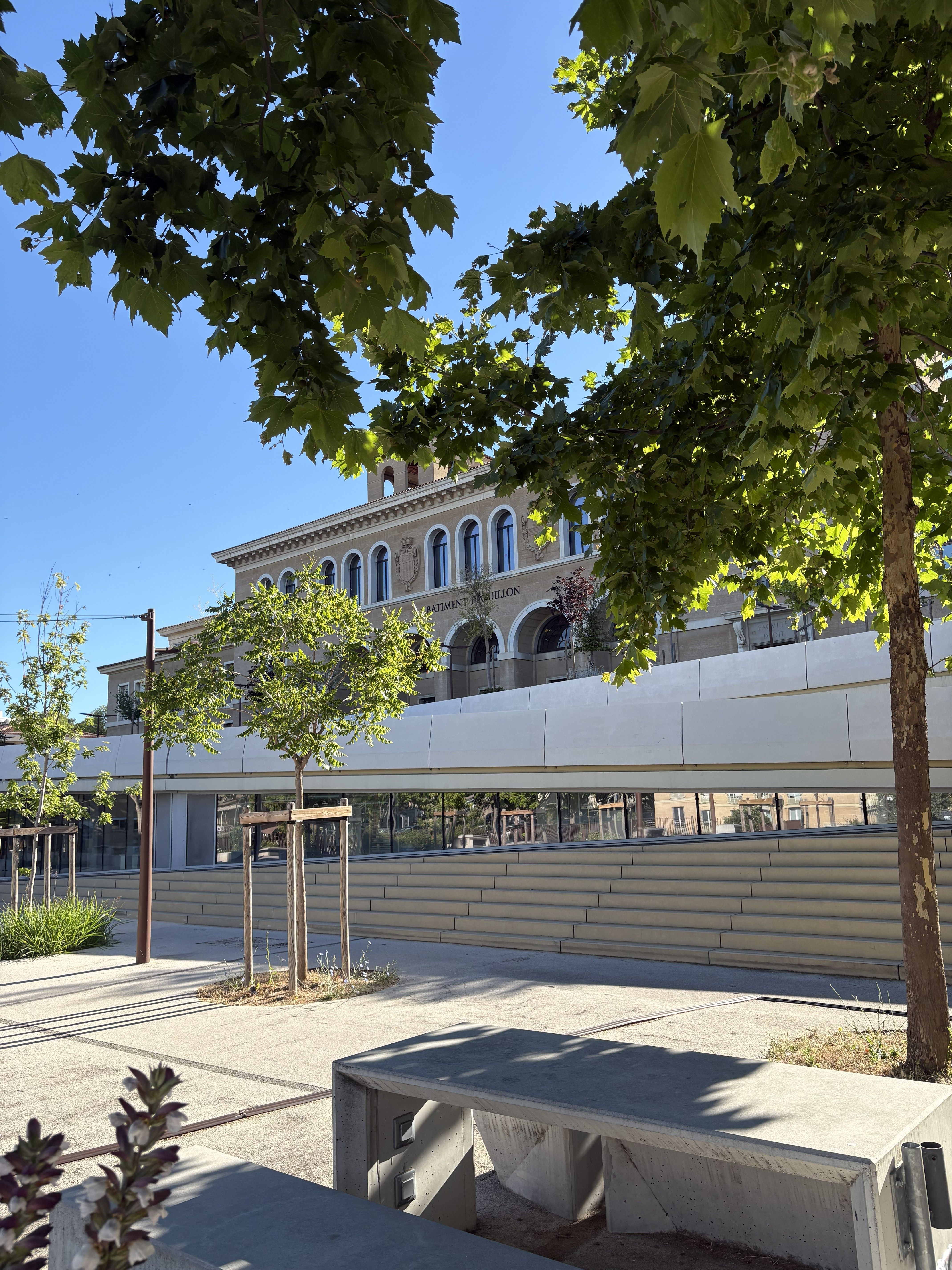 Blick auf den Campus Schuman der Aix-Marseille Université in Aix-en-Provence mit Bäumen, Sitzflächen und Universitätsgebäude.