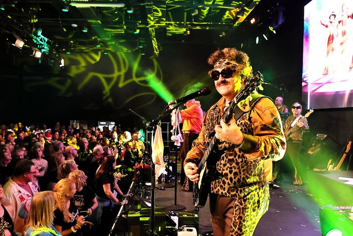 Weitwinkel: Bühne mit Performer und dichtem Publikum, Lichtshow im Saal.