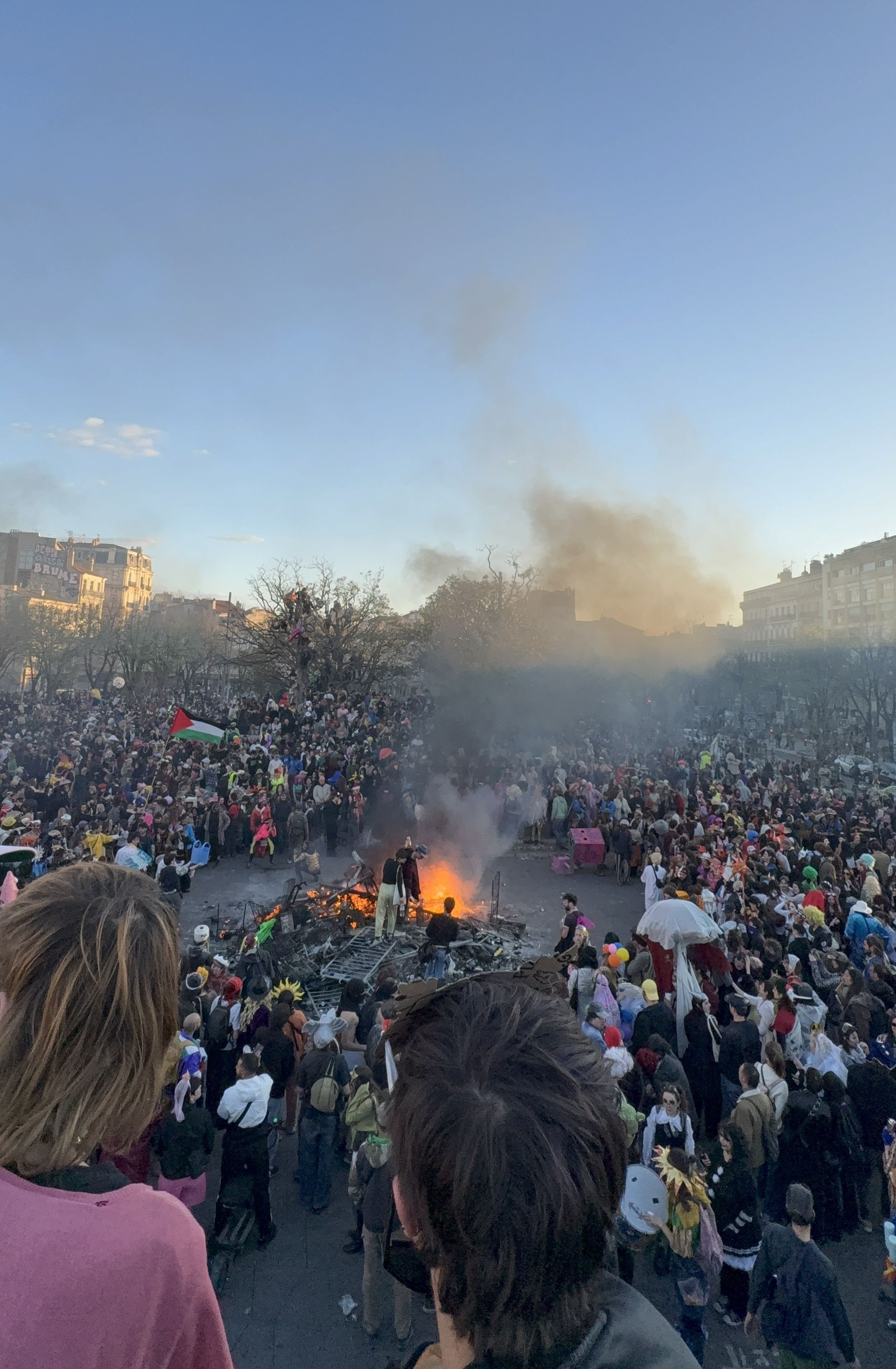 Große Menschenmenge beim Carnaval de Marseille auf La Plaine, mit Rauch und Feuer in der Mitte des Platzes.
