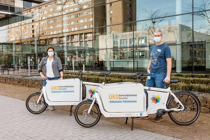 Foto:©  Um im Großstadt-Dschungel von Düsseldorf überall schnell und bequem hinzukommen, betreut das SAPV-Team der Uniklinik Düsseldorf die Patientinnen und Patienten mit einem Fuhrpark aus Elektrofahrzeugen. Das ist umweltschonend und sorgt dafür, dass man überall einen Parkplatz bekommt. Seit Februar neu dabei: Ein zweites Elektro-Lastenfahrrad. (Foto: Universitätsklinikum Düsseldorf/UKD)