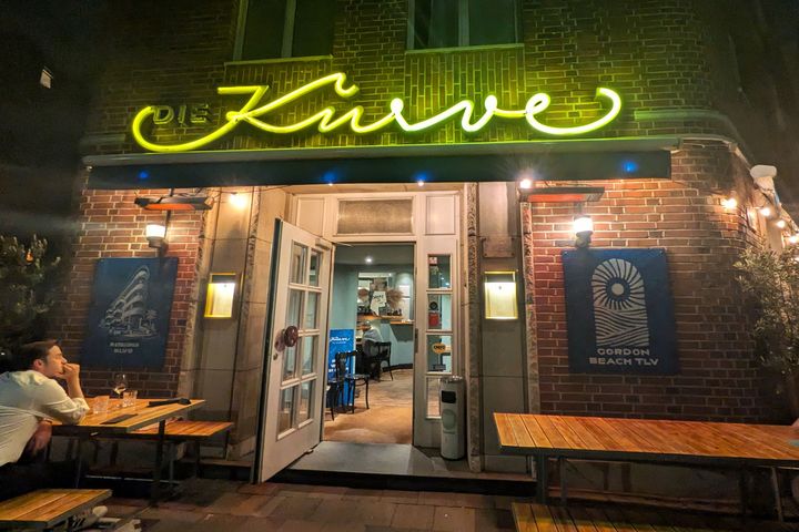Beleuchtete Backsteinfassade des Restaurants Die Kurve an der Goebenstraße in Düsseldorf-Pempelfort mit gelbem Neonschriftzug und geöffnetem Eingang.