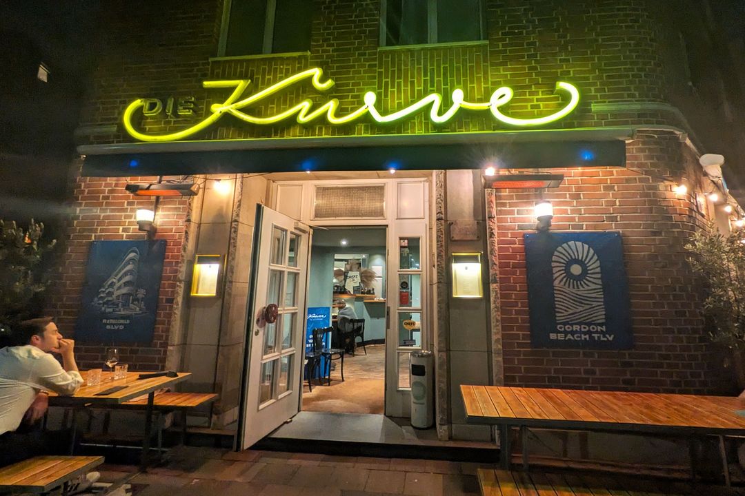 Beleuchtete Backsteinfassade des Restaurants Die Kurve an der Goebenstraße in Düsseldorf-Pempelfort mit gelbem Neonschriftzug und geöffnetem Eingang.