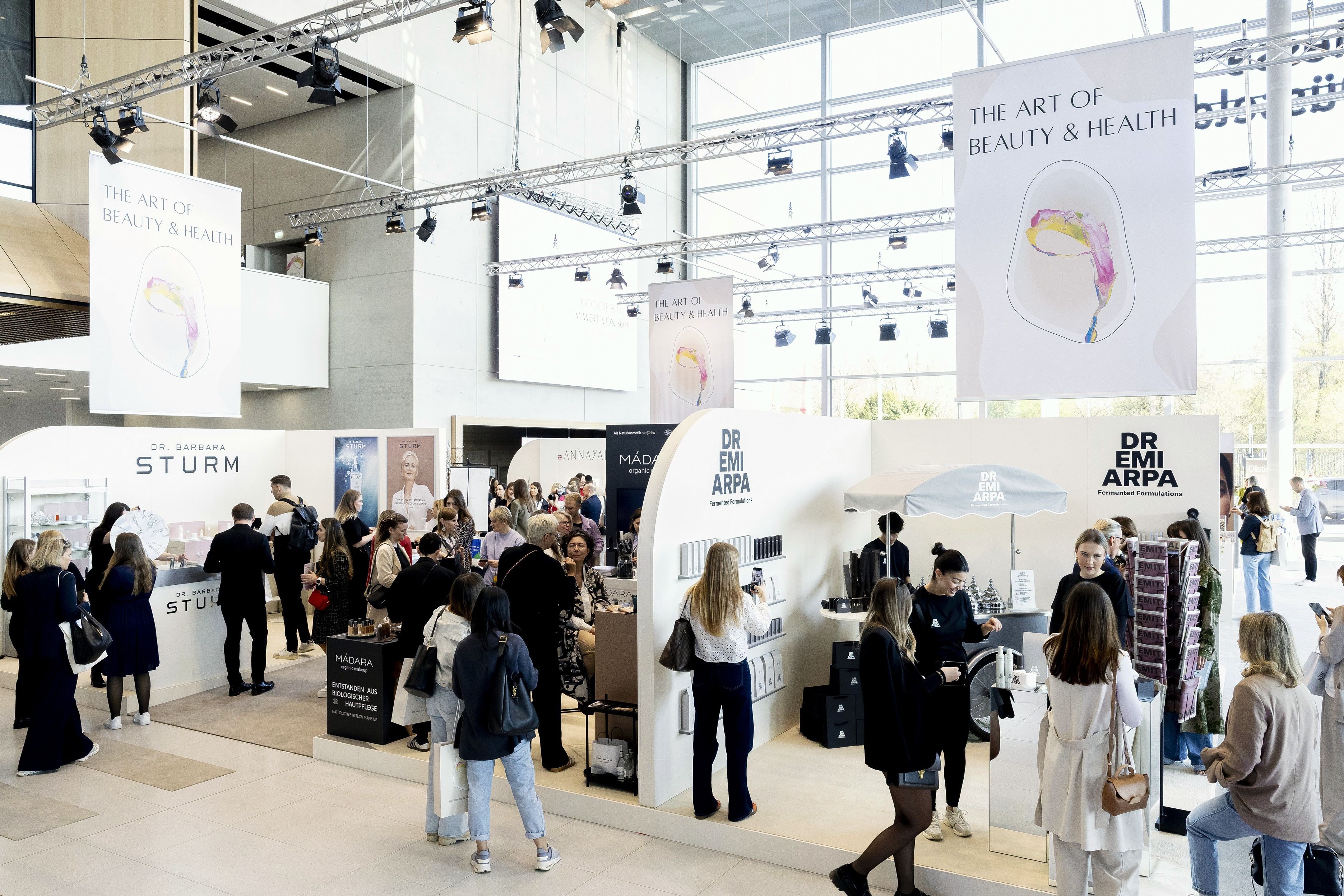 Besucherinnen und Besucher an Markenständen im Glasfoyer der Messe Düsseldorf bei The Art of Beauty & Health.