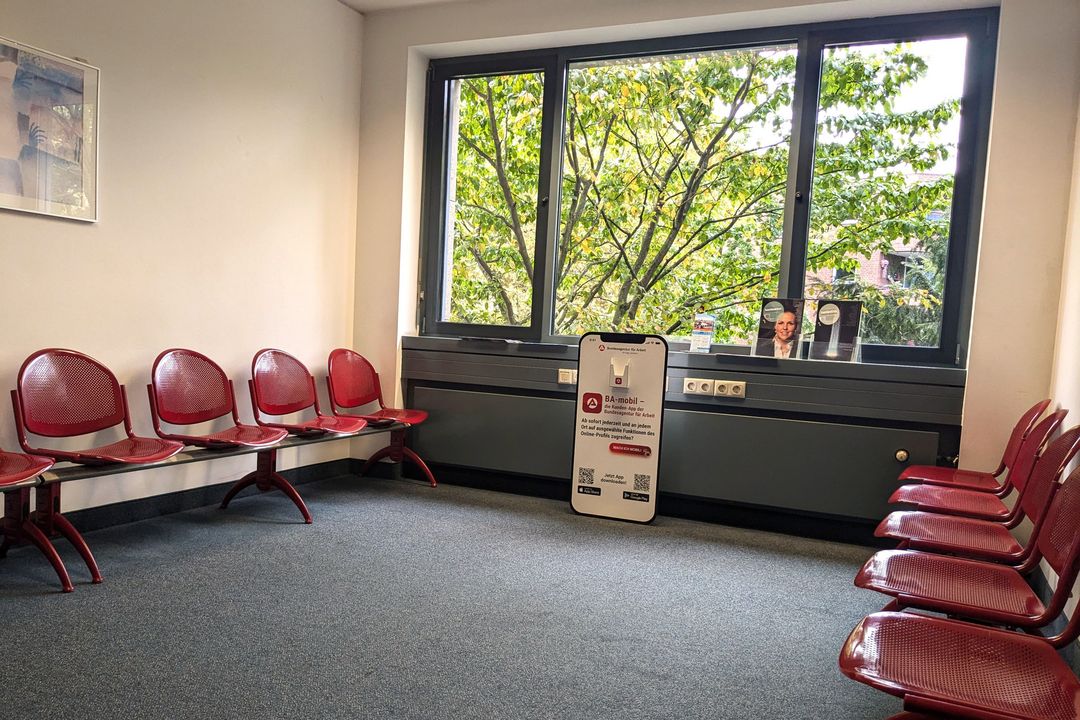 Wartebereich der Agentur für Arbeit Düsseldorf mit roten Stühlen und Hinweisschild zur digitalen Beratung