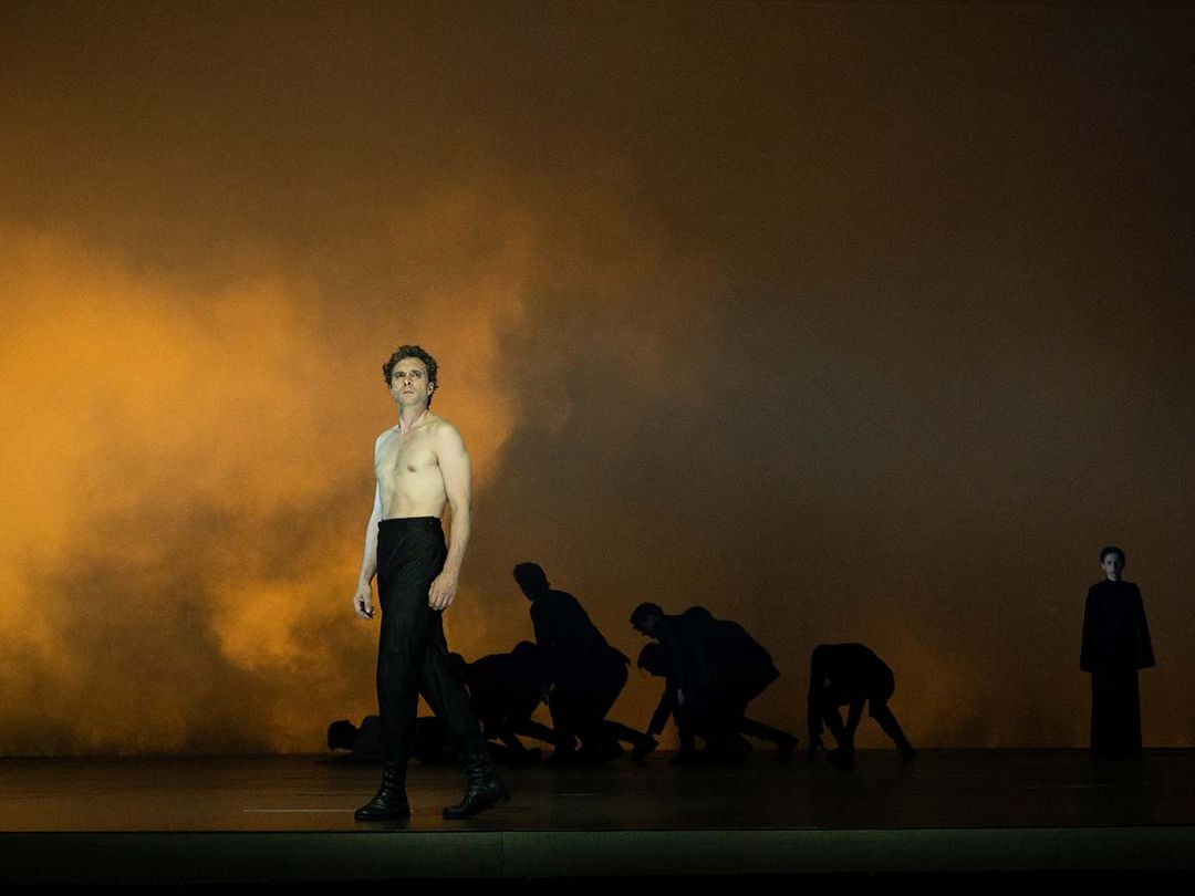 Prinz Friedrich von Homburg am Düsseldorfer Schauspielhaus André Kaczmarczyk steht mit nacktem Oberkörper vor dem gebückten Ensemble auf einer ockergelb beleuchteten, von Nebel erfüllten Bühne.
