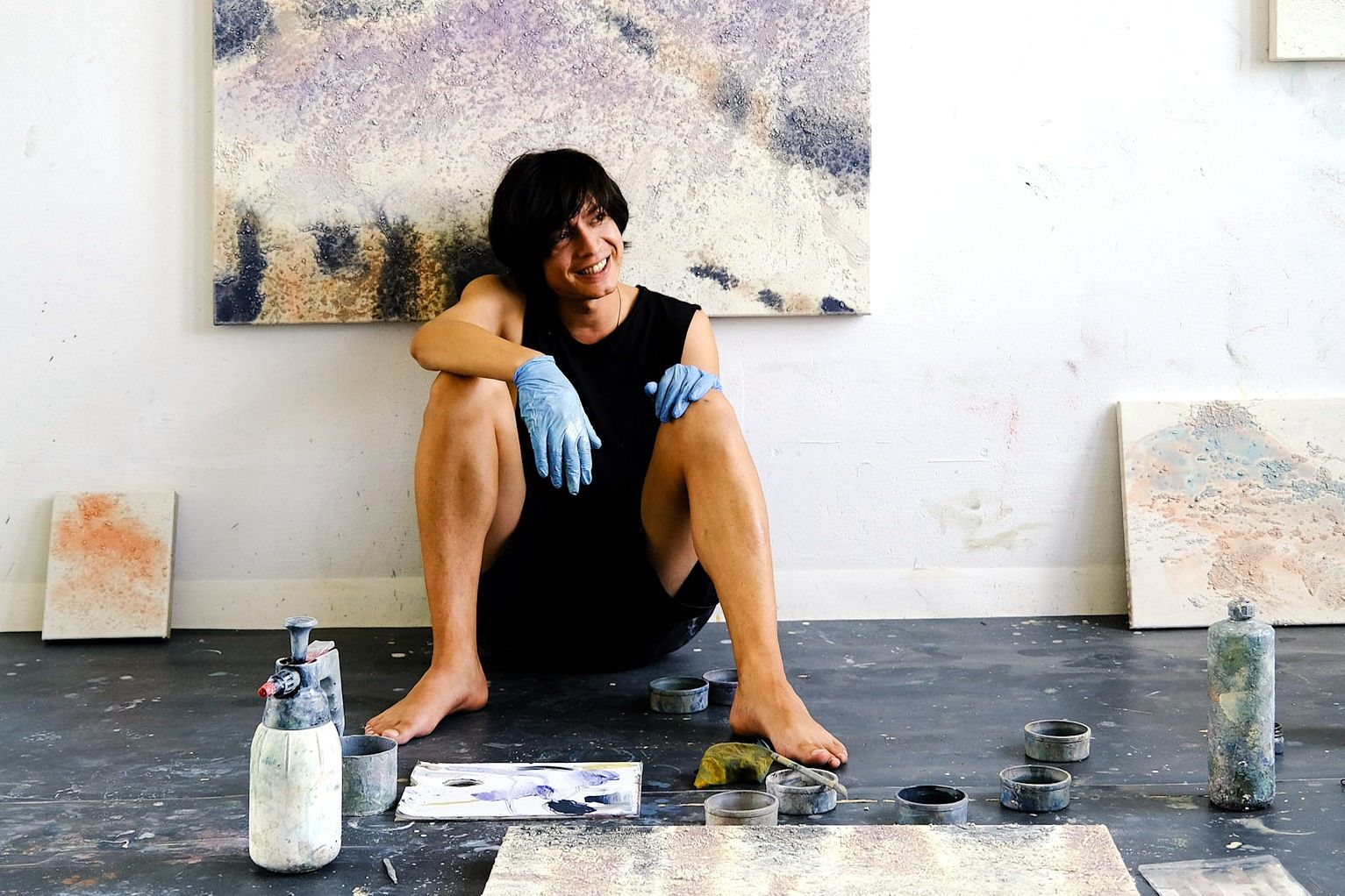 Künstler Matthias Jun Wilhelm sitzt in seinem Atelier, umgeben von Leinwänden und Malutensilien.