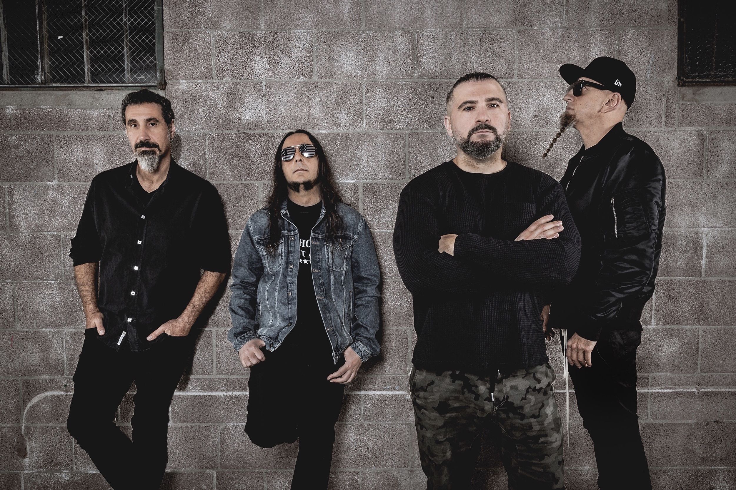Pressefoto der Band System Of A Down vor einer grauen Betonwand.