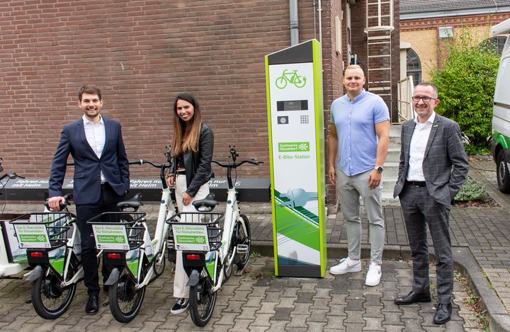 Tobias Meurer (Co-Founder & CIO Velocity, Alina Bauer (Head of Customer Journey Velocity), Fabian Sklorz (Entwicklung neuer Geschäftsmodelle Stadtwerke Düsseldorf) und Eckart Birkenkamp (Leiter Wohnungs- und Immobilienwirtschaft Vertrieb Stadtwerke Düsseldorf) an einer der E-Bike-Stationen der Stadtwerke Düsseldorf.