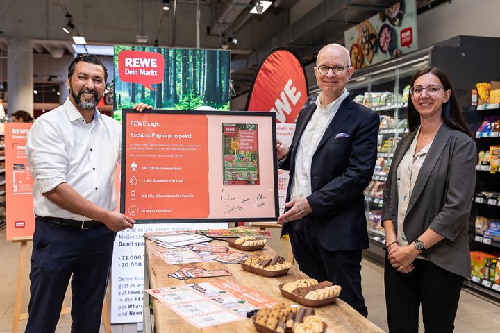 REWE-Kaufmann Yassine Fakhouri, Hanno Rieger, Vorsitzender der Geschäftsleitung REWE Region West und Carina Peretzke, Handelsverband Nordrhein-Westfalen, hingen den gerahmten Papier-Prospekt gemeinsam an den Nagel/ Foto: REWE, Yassine Fakhouri 