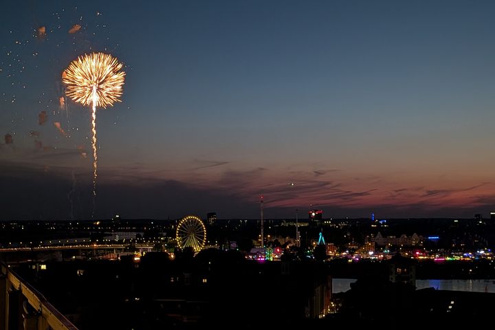 Feuerwerk über der Düsseldorfer Rheinkirmes Blick über Düsseldorf auf die beleuchtete Rheinkirmes auf den Oberkasseler Rheinwiesen. Links steigt ein Feuerwerk in den Abendhimmel, darunter sind das Riesenrad und weitere Fahrgeschäfte zu sehen.