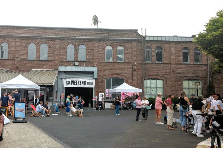Hof der Elegant Elephant Studios in Düsseldorf-Lierenfeld beim Loft of Art Weekend Vol. 5, Besucher und Stände unter einem Banner mit der Aufschrift Loft of Art Weekend.