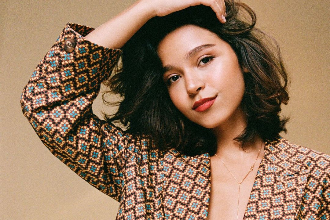 Porträt der brasilianischen Sängerin Mari Froes in gemustertem Blazer vor beigem Hintergrund.