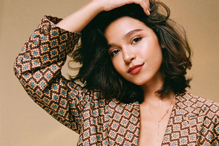 Porträt der brasilianischen Sängerin Mari Froes in gemustertem Blazer vor beigem Hintergrund.