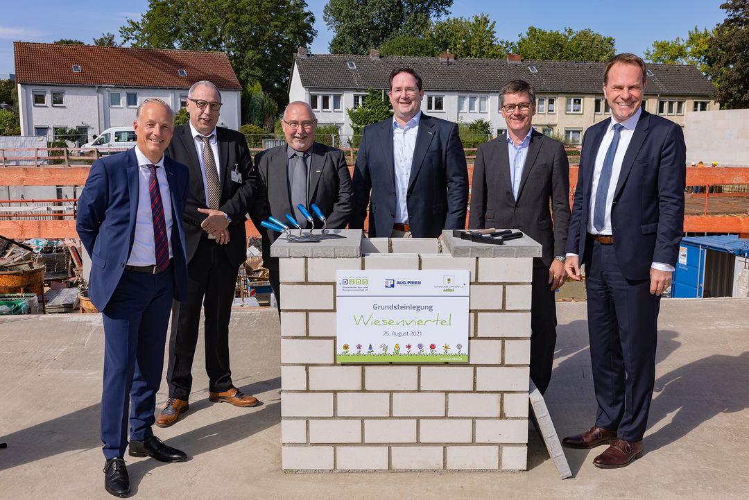 Alexander Rychter (Direktor des Verbandes der Wohnungswirtschaft Rheinland Westfalen), Rolf Meven (Aufsichtsratsvorsitzender der DüBS), Frank H. Adolphs (Vorstandsmitglied der DüBS), Niels Klein (Vorstandssprecher der DüBS), Michael Groß (Geschäftsführer des Bauunternehmens August Prien) und Oberbürgermeister Dr. Stephan Keller versenken die Zeitkapsel im Grundstein des Sonnenblumenfelds der DüBS (v.l.n.r.).