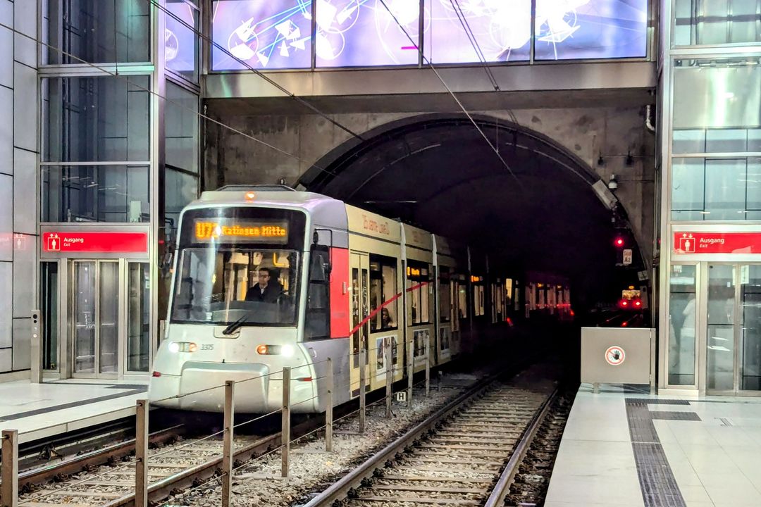 Einfahrende Rheinbahn‑Stadtbahn an einer Düsseldorfer U‑Bahn‑Station mit Tunnel, Gleisen und Bahnsteig.