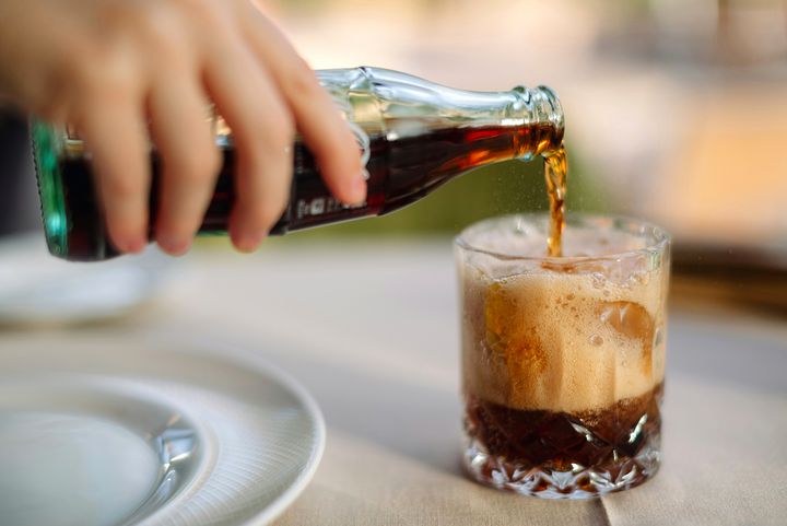 Cola wird in ein Glas gegossen Hand gießt Cola aus einer Glasflasche in ein Glas mit Eiswürfeln