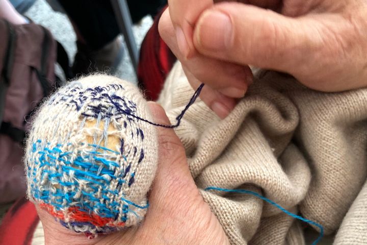 Hände reparieren einen hellen Strickpullover mit blauem Garn und einem Stopfei