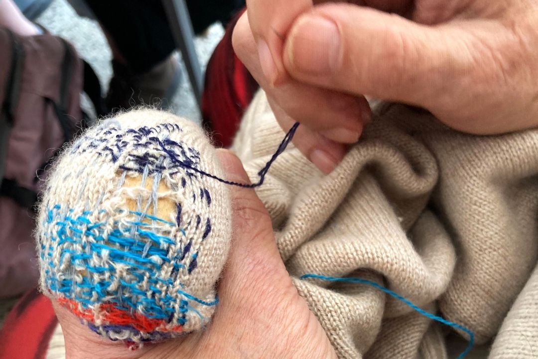 Hände reparieren einen hellen Strickpullover mit blauem Garn und einem Stopfei
