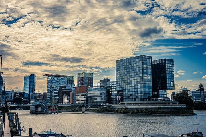 Blick über den Rhein auf moderne Büro- und Hotelgebäude im Düsseldorfer MedienHafen unter bewölktem Himmel.