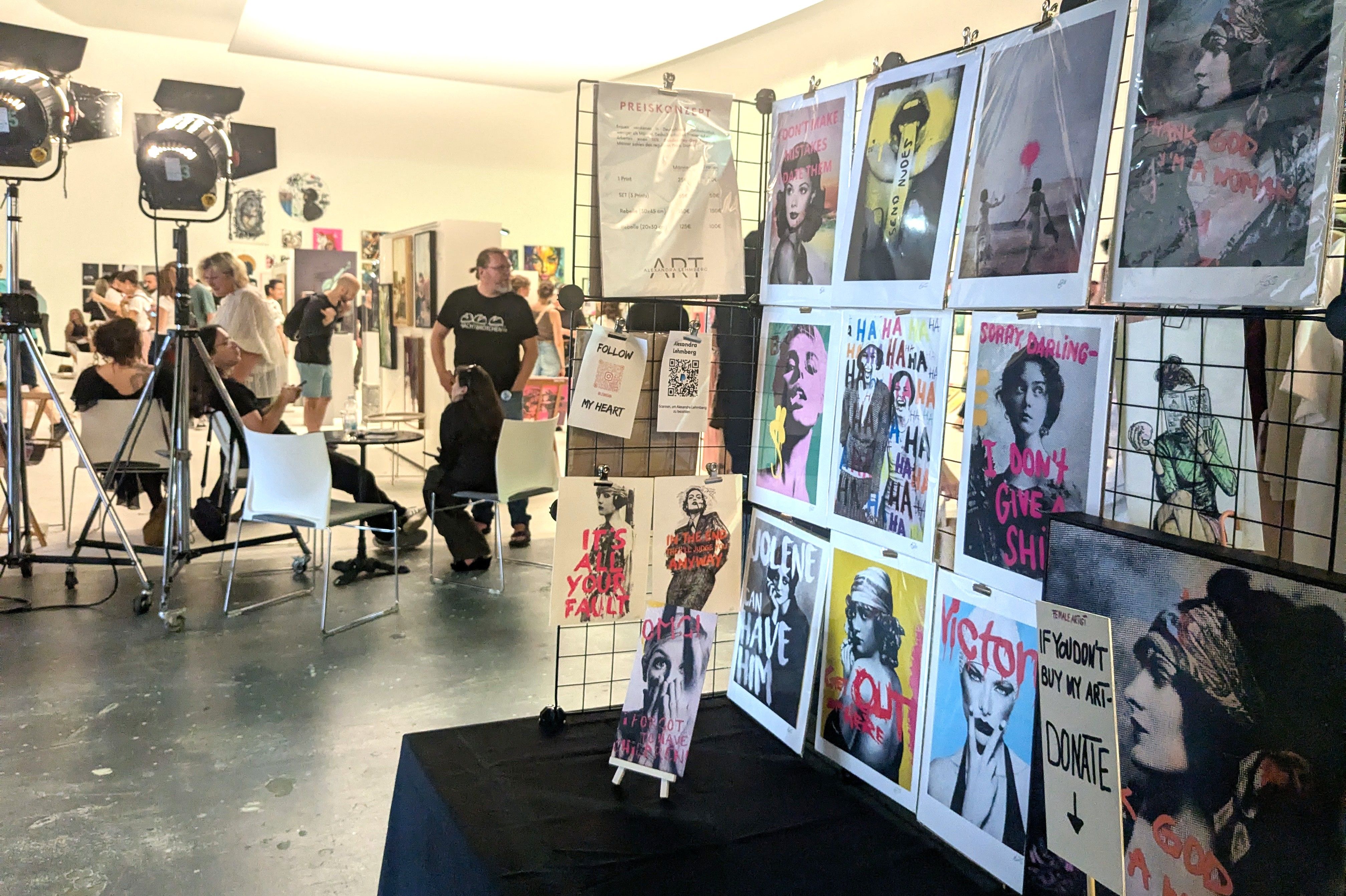 Stand mit gerahmten Prints feministischer Motive, daneben Preisliste und QR-Code mit dem Namen Alexandra Lehmberg.