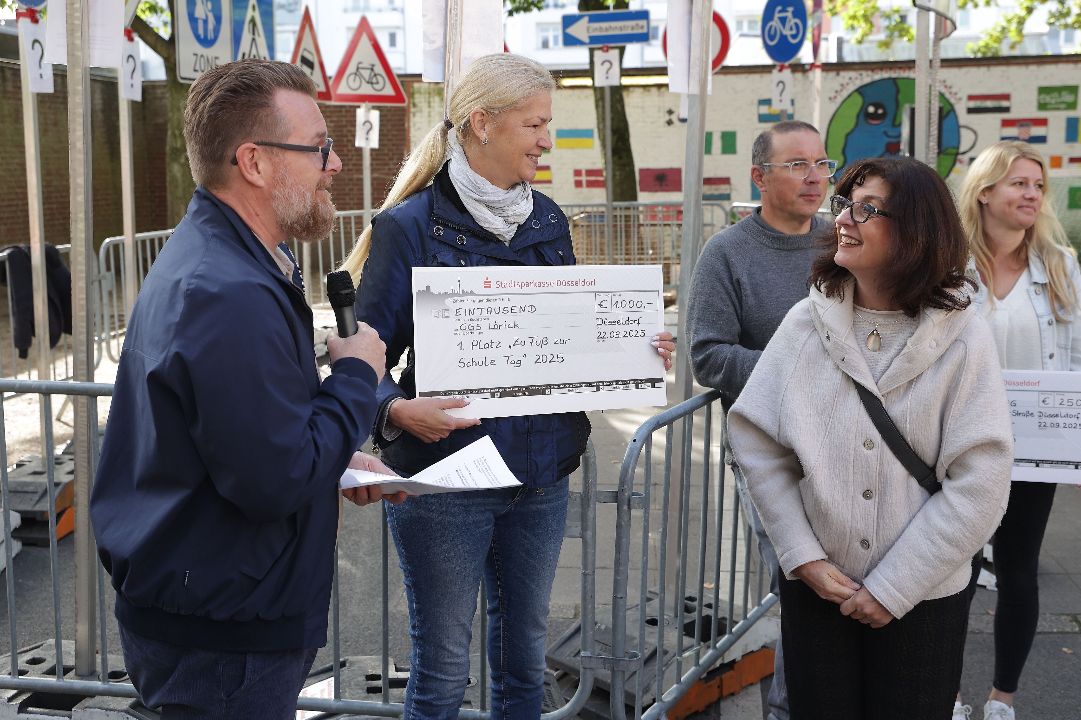 Benjamin Sack, Mobilitätsdezernat, und Antonia Schnelle, Amt für Verkehrsmanagement, überreichten den ersten Preis an Gabriele Cunrady von der Gemeinschaftsgrundschule Lörick (vorne, v.l.). Im Hintergrund Jens Böhm, Leiter der GGS Lennéstraße und Dina Kirschbaum von der Katholischen Fleher Schule. / Foto: Landeshauptstadt Düsseldorf/David Young