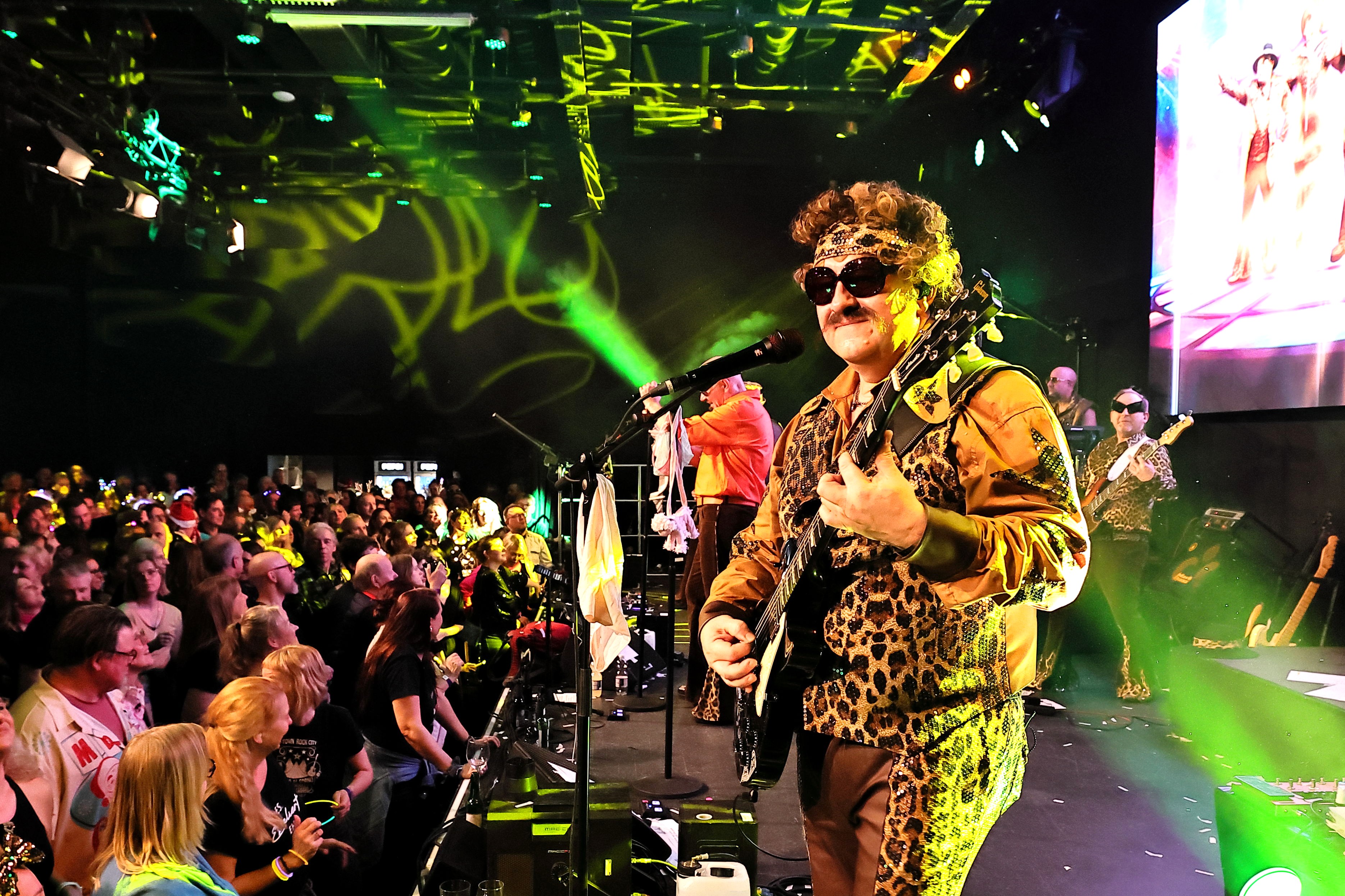 Porno al Forno live auf der Bühne: Gitarrist Bobaus Texas spielt vor vollem Saal, Blick ins Publikum (Düsseldorf, 20.12.2025).