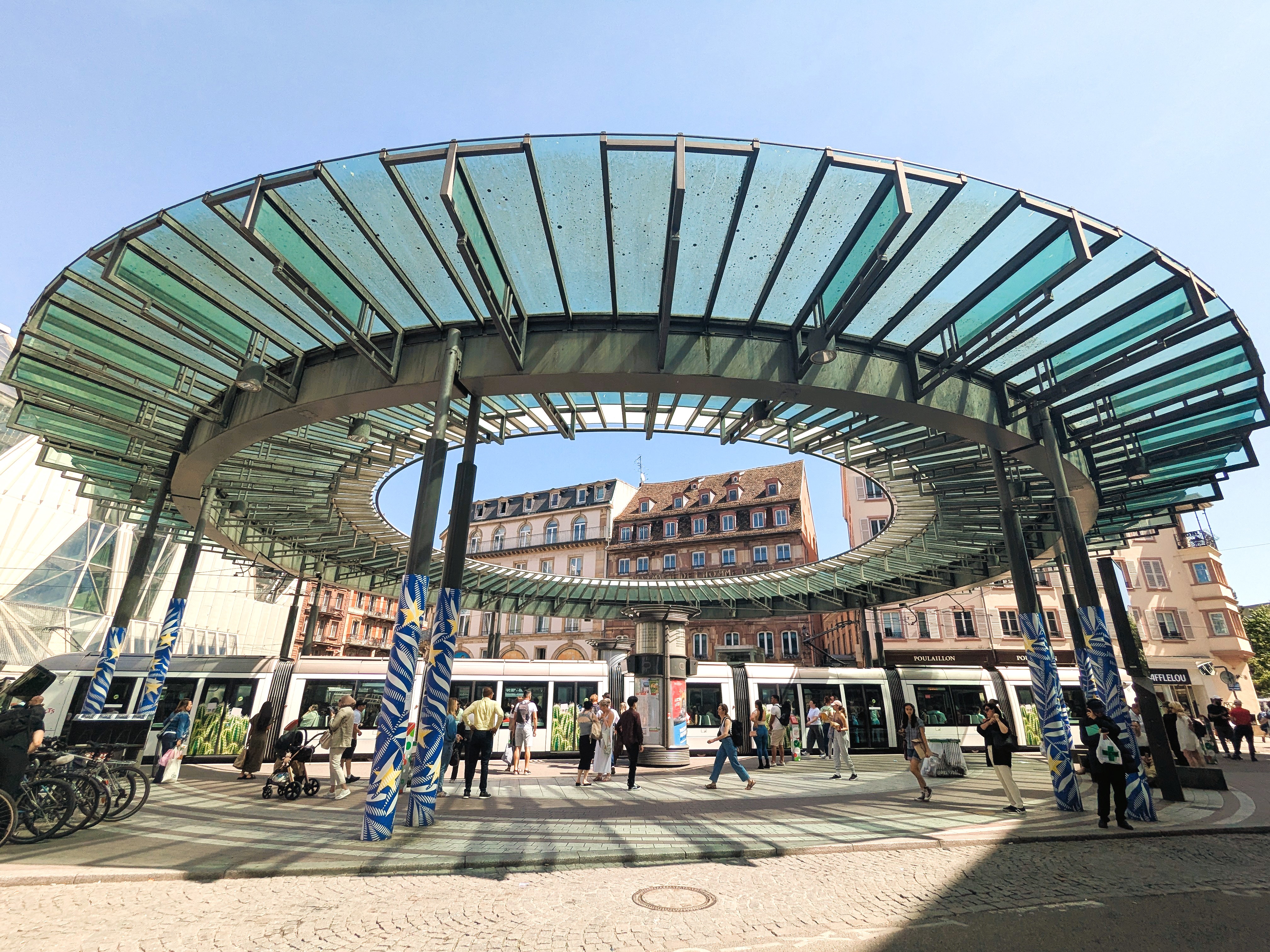 Place Kléber in Straßburg mit großer Glasüberdachung, Tram und Passanten bei Sonnenschein.