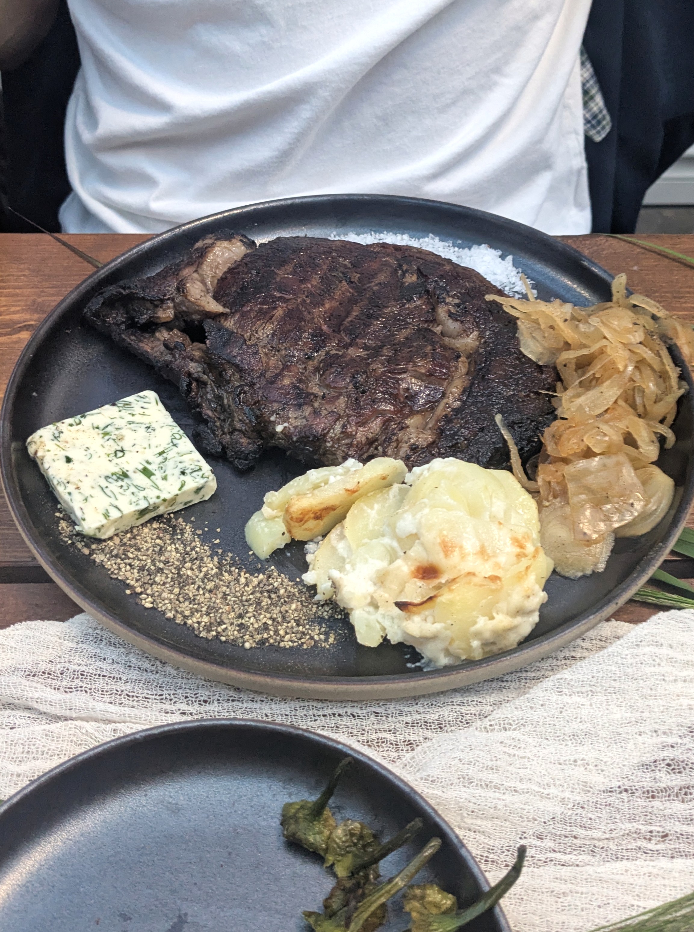 Ribeye auf dem Teller – gut gebraten, begleitet von Zwiebeln, Pfeffer, Kartoffelgratin und Kräuterbutter. / Foto: Alexandra Scholz-Marcovich, NDOZ