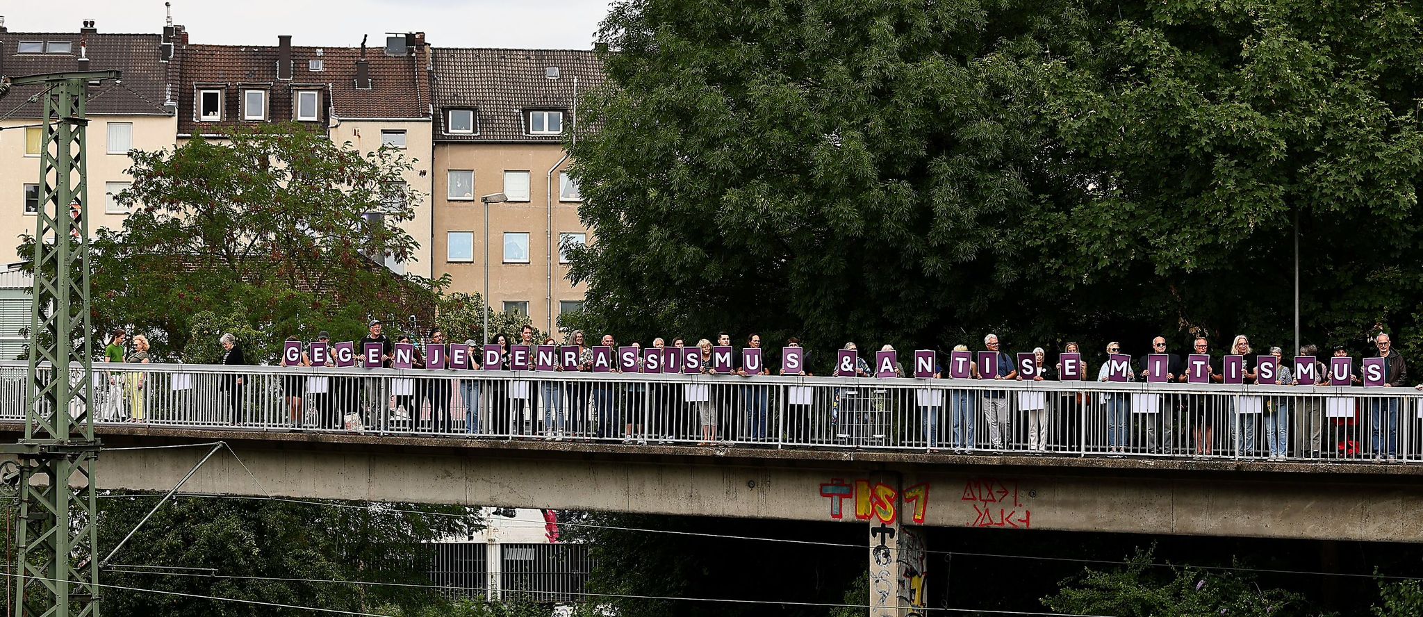 Mit großen Buchstaben positionierten sich Teilnehmende der Gedenkveranstaltung auf der Brücke am Wehrhahn: „Gegen jeden Rassismus & Antisemitismus“ – ein sichtbares Zeichen der Solidarität. / Foto: Klaus von Jackelmann