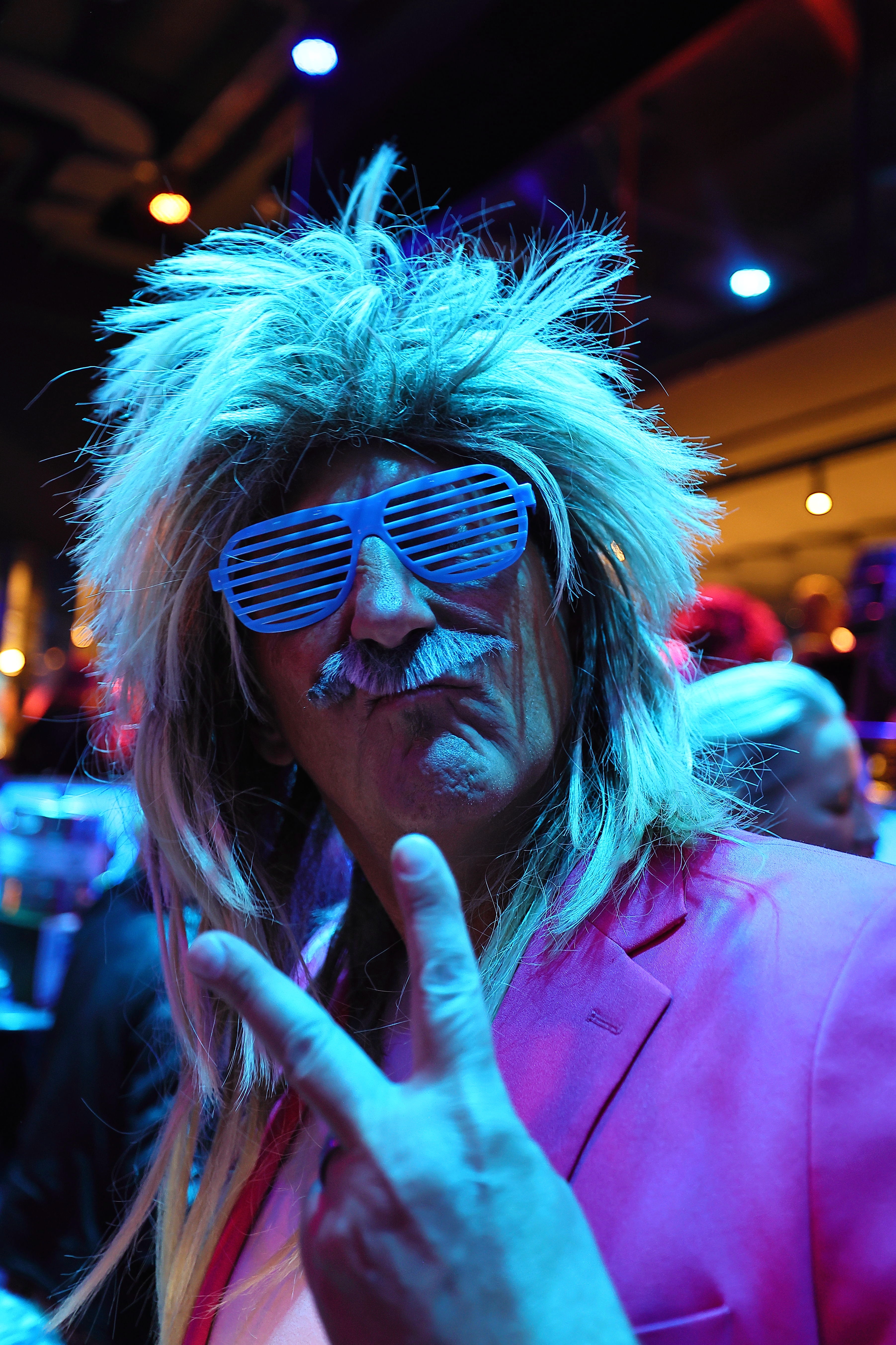 Person mit blauer Perücke und Sonnenbrille zeigt ein Peace-Zeichen.