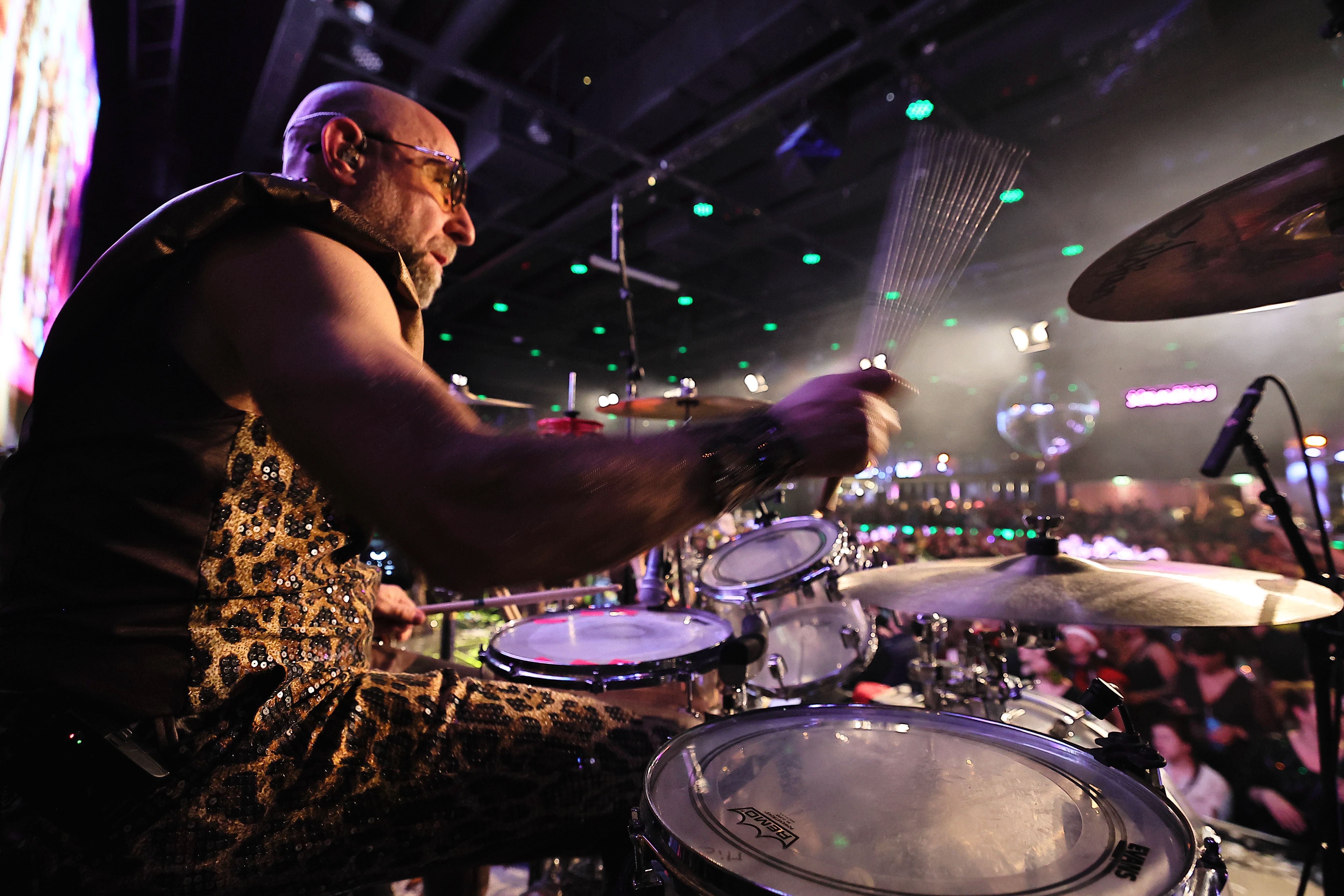 Schlagzeuger spielt, Drumset im Vordergrund, Publikum und Deckenlichter dahinter.