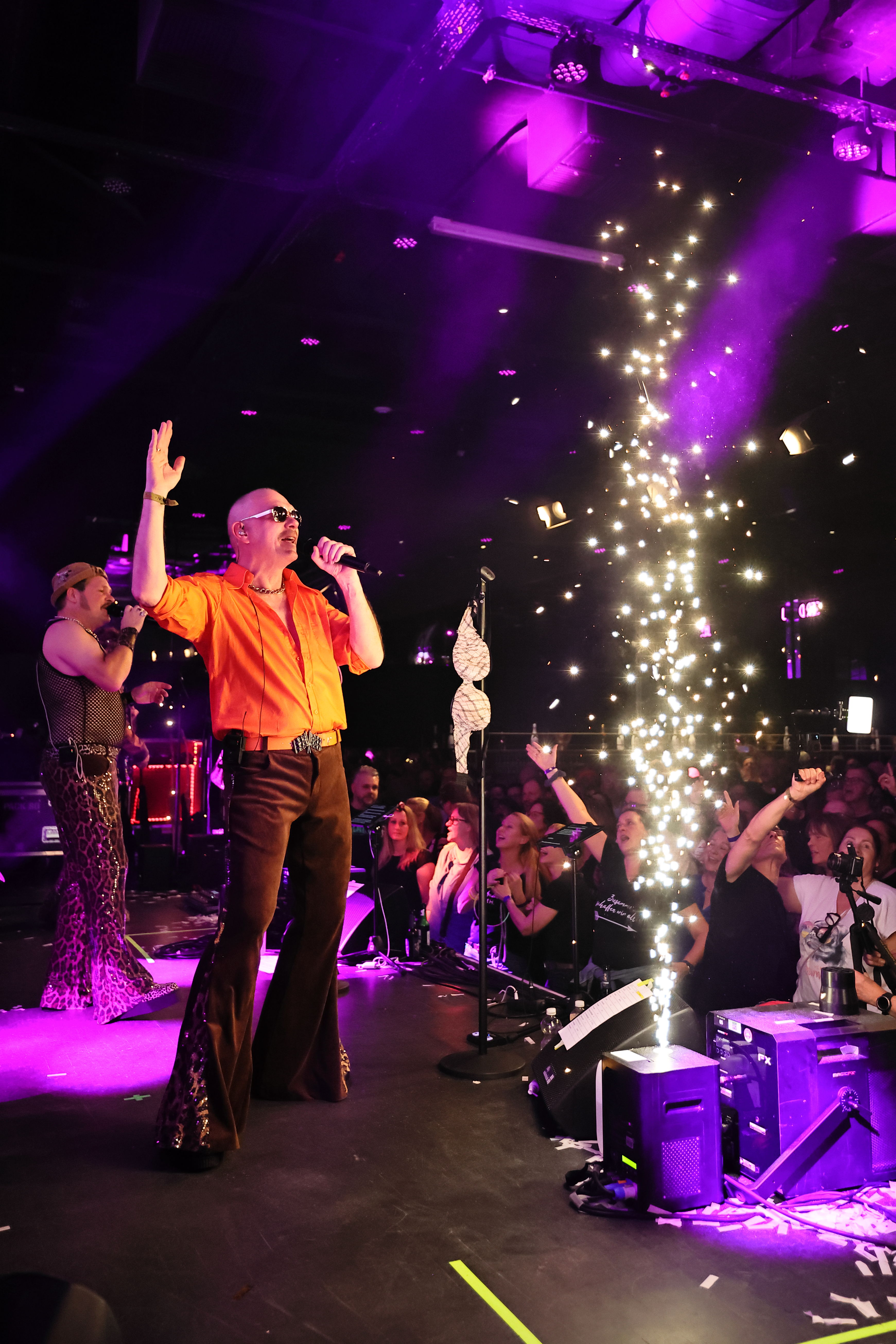 Sänger auf der Bühne neben Funkenfontäne, violettes Bühnenlicht.